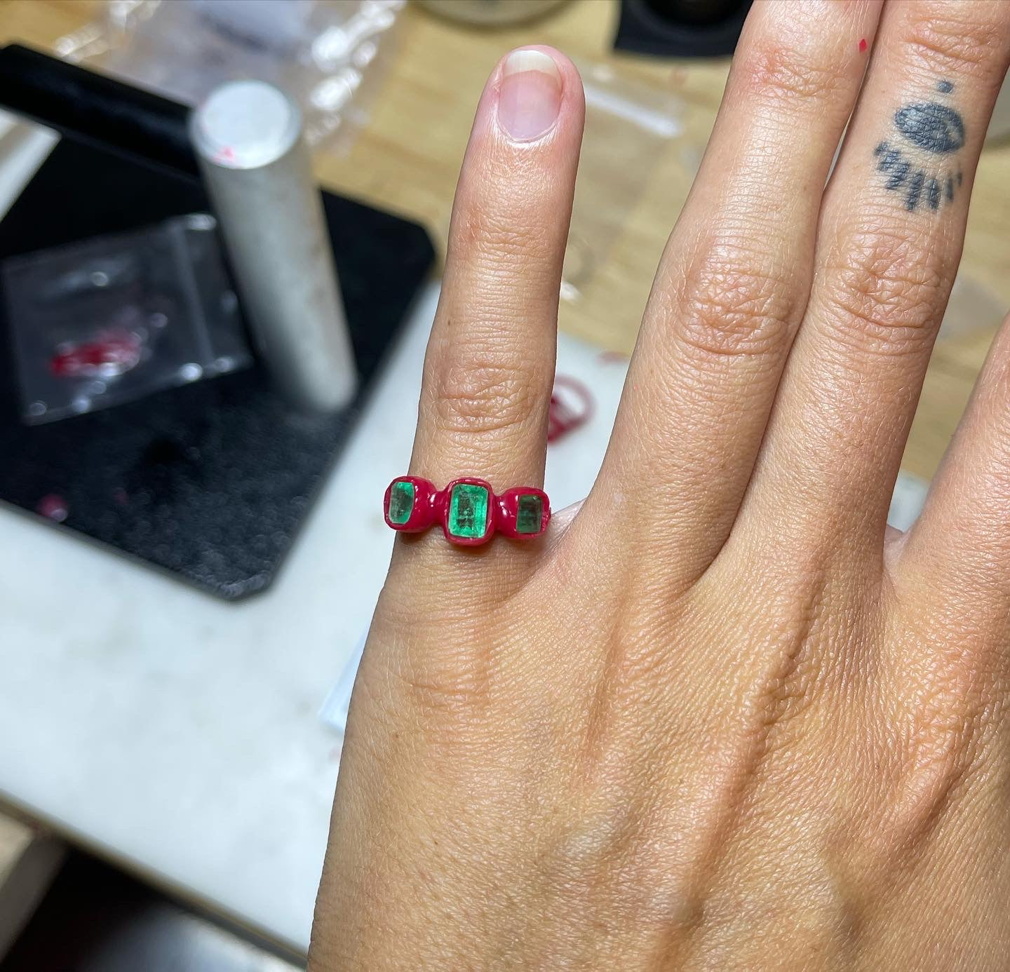 An emerald trio ring in its wax stage is worn to show what it looks like before it is cast in gold.