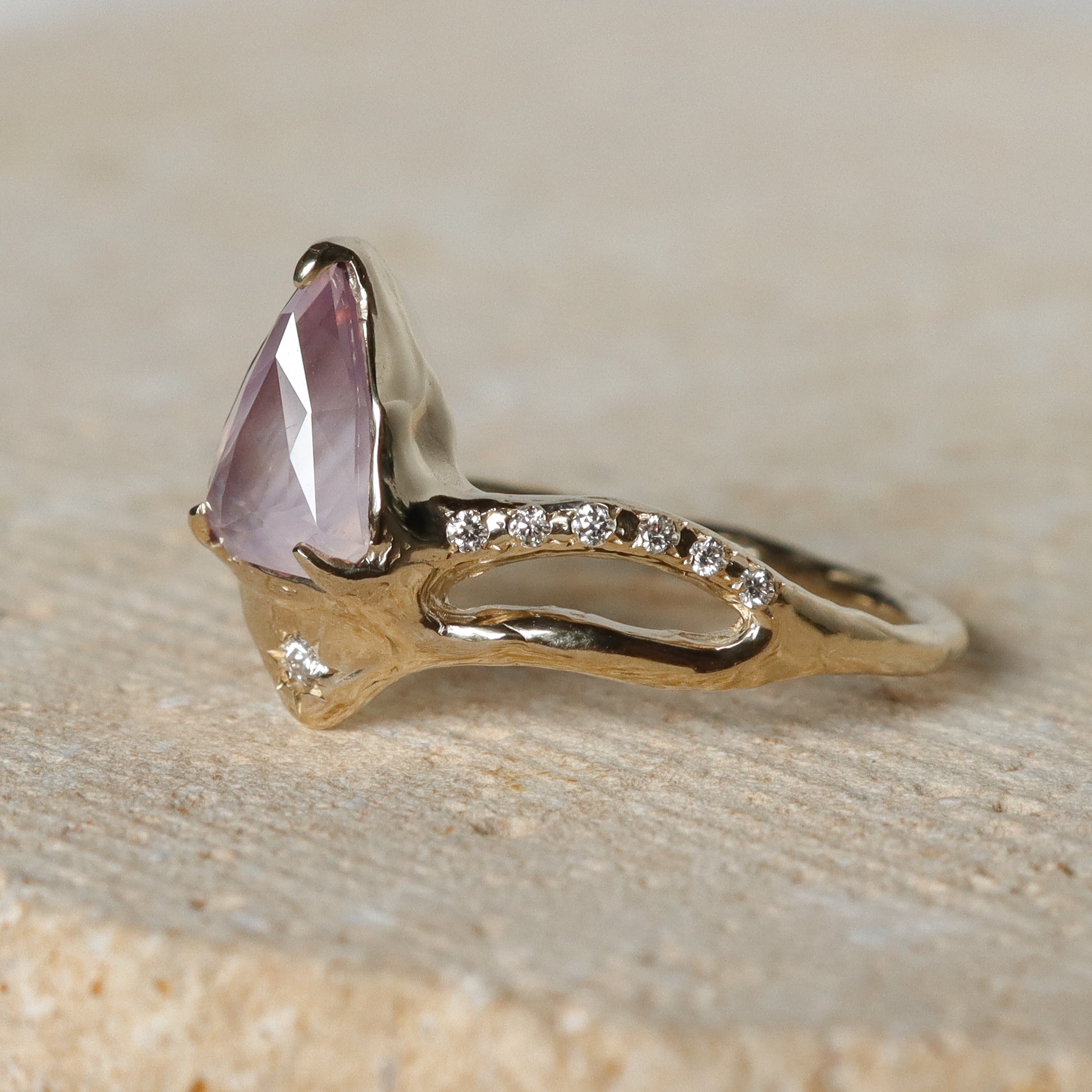 Gold ring with a pink gemstone on a beige surface