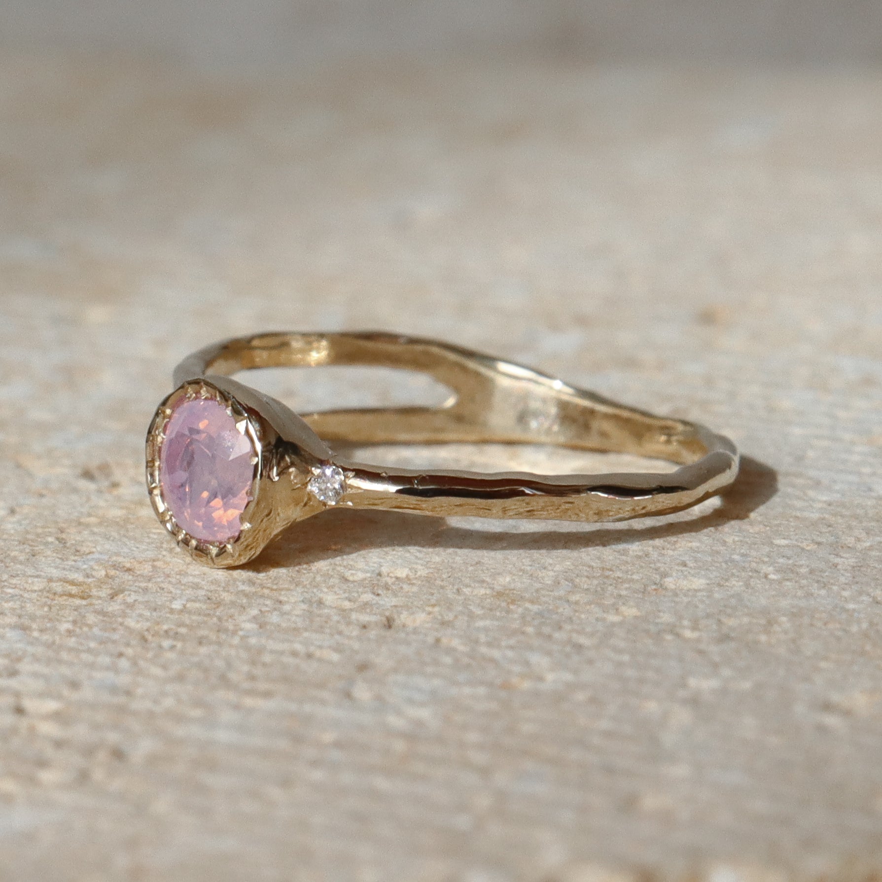 Gold ring with a pink gemstone on a beige surface