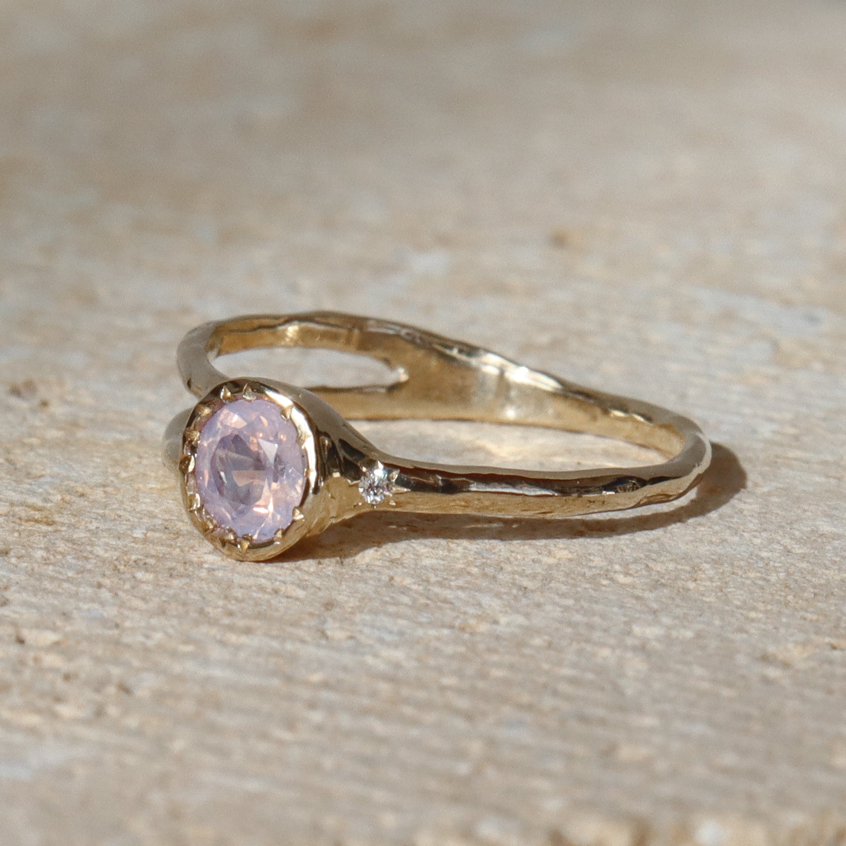 Gold ring with a pink gemstone on a beige surface