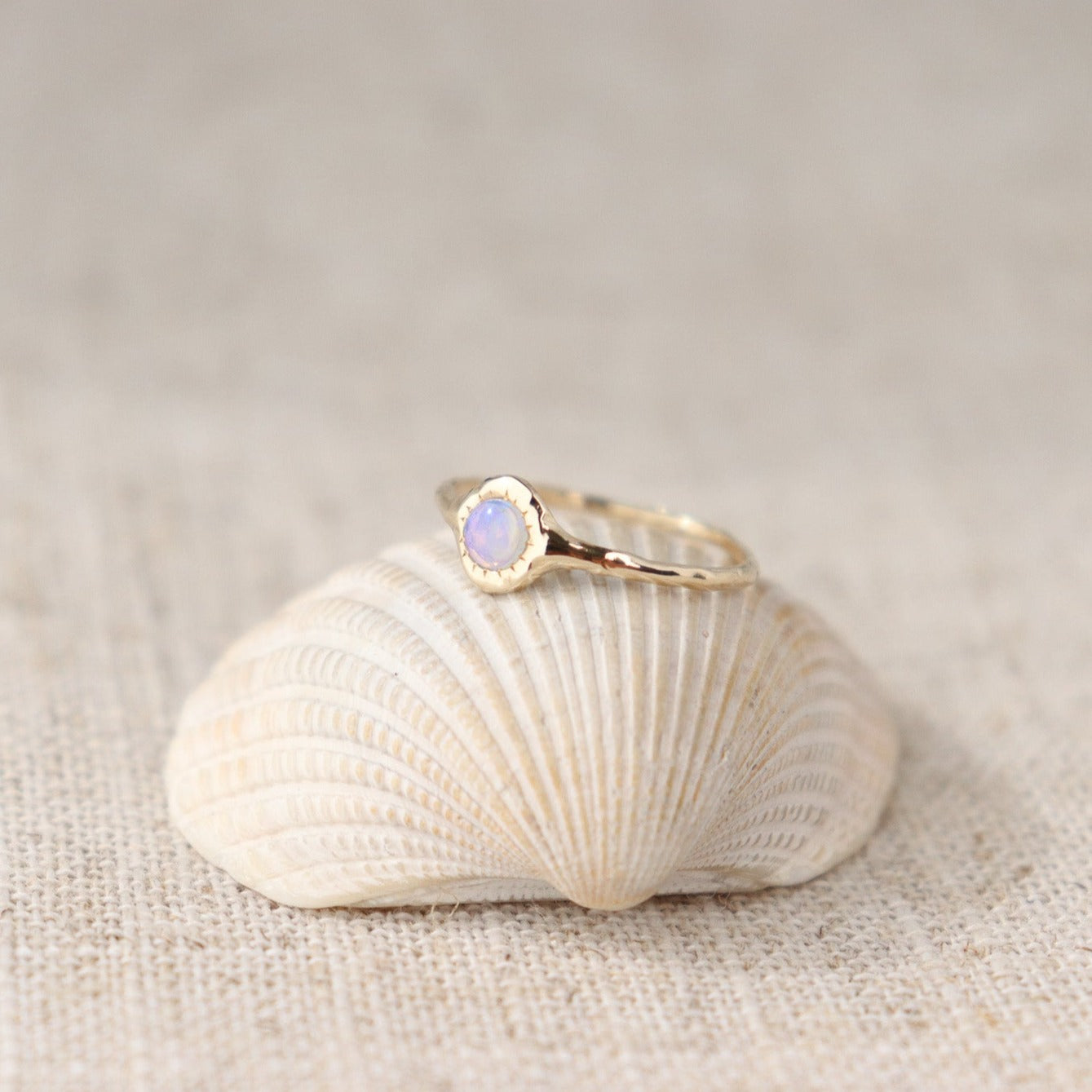 A round opal ring, set on a slender band with small tick-like accents that radiate like a starburst, creating a mesmerizing and celestial jewelry piece.