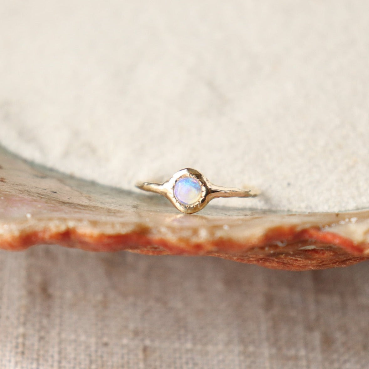 A round opal ring, set on a slender band with small tick-like accents that radiate like a starburst, creating a mesmerizing and celestial jewelry piece.