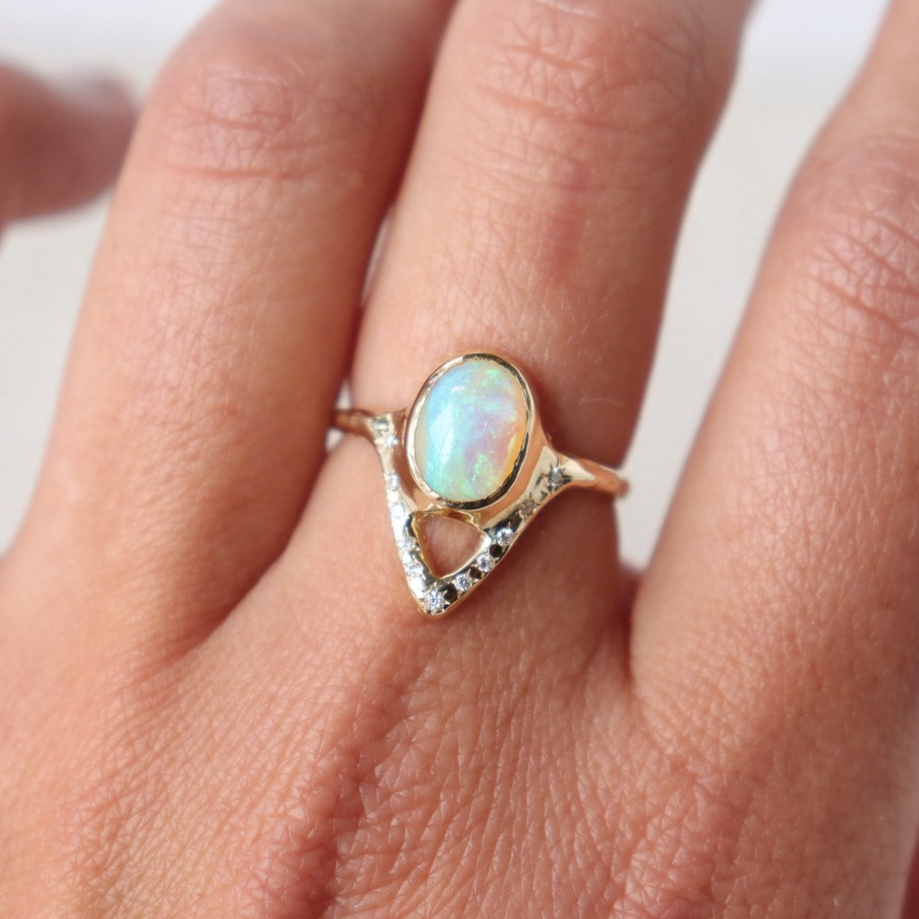 Elegant opal ring featuring a V-shaped design adorned with sparkling diamond accents, shown on a finger for scale.