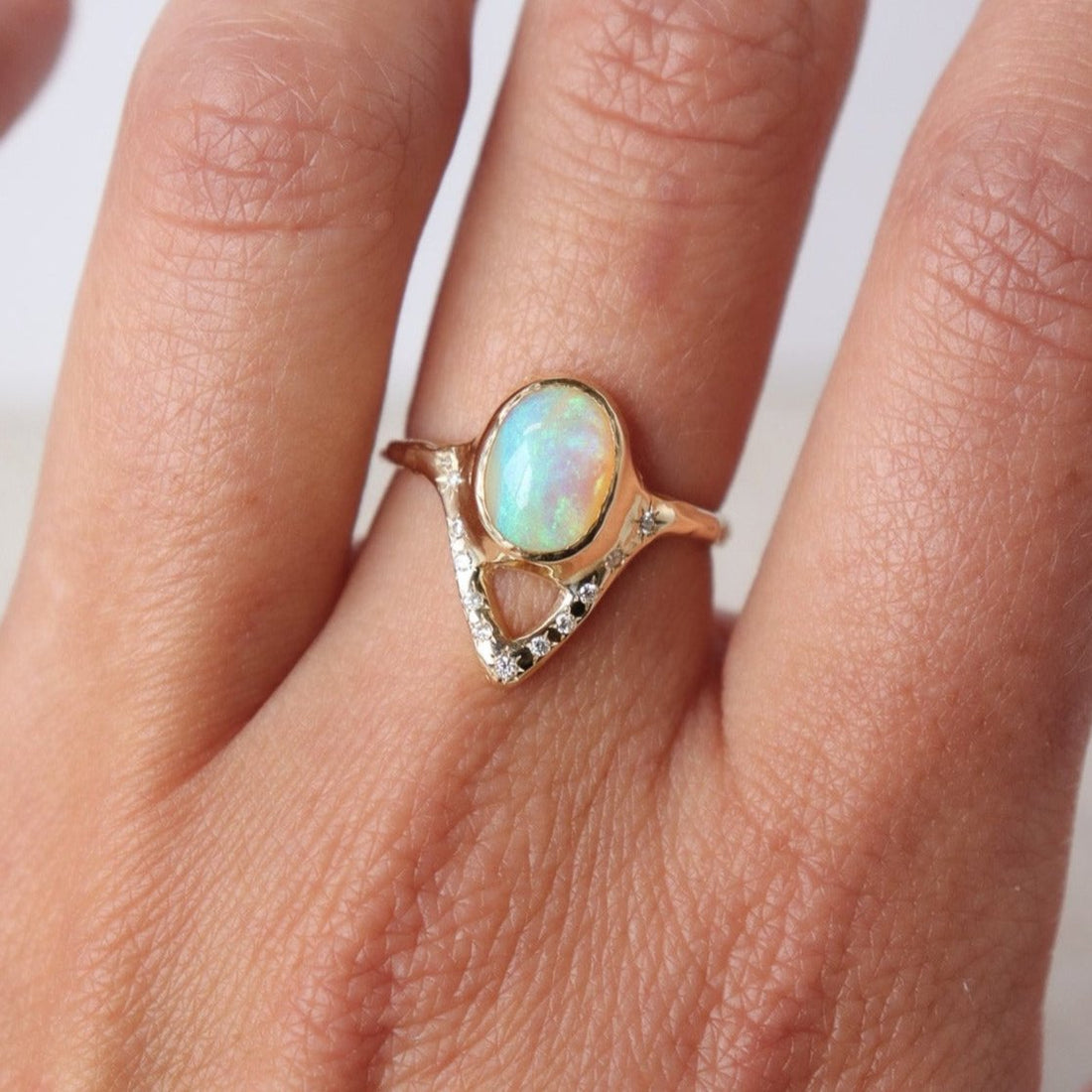 Elegant opal ring featuring a V-shaped design adorned with sparkling diamond accents, shown on a finger for scale