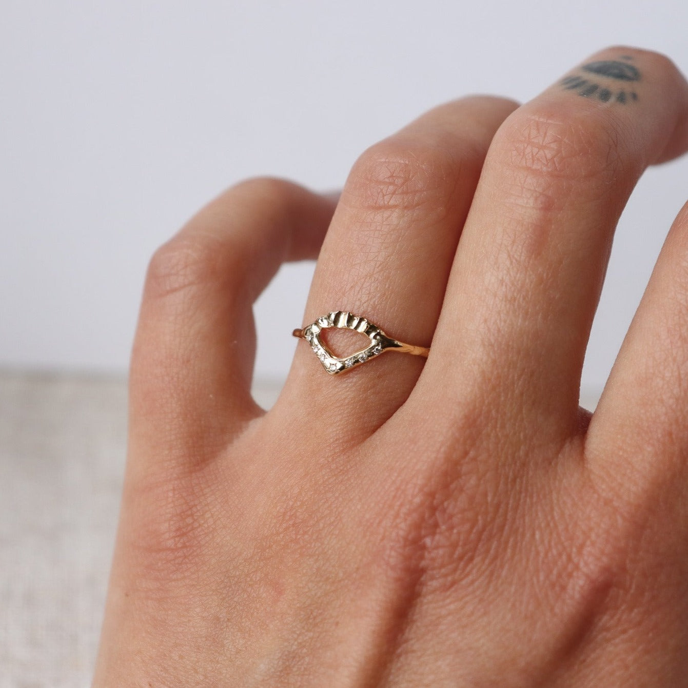 Elegant gold ring with V-shaped diamond detail and arched fin texture, worn to show texture.