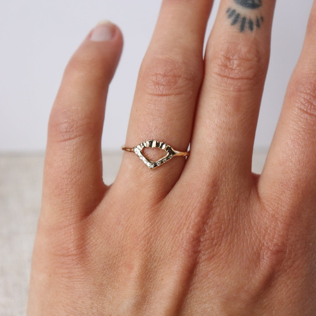 Elegant gold ring with V-shaped diamond detail and arched fin texture, worn to show texture.