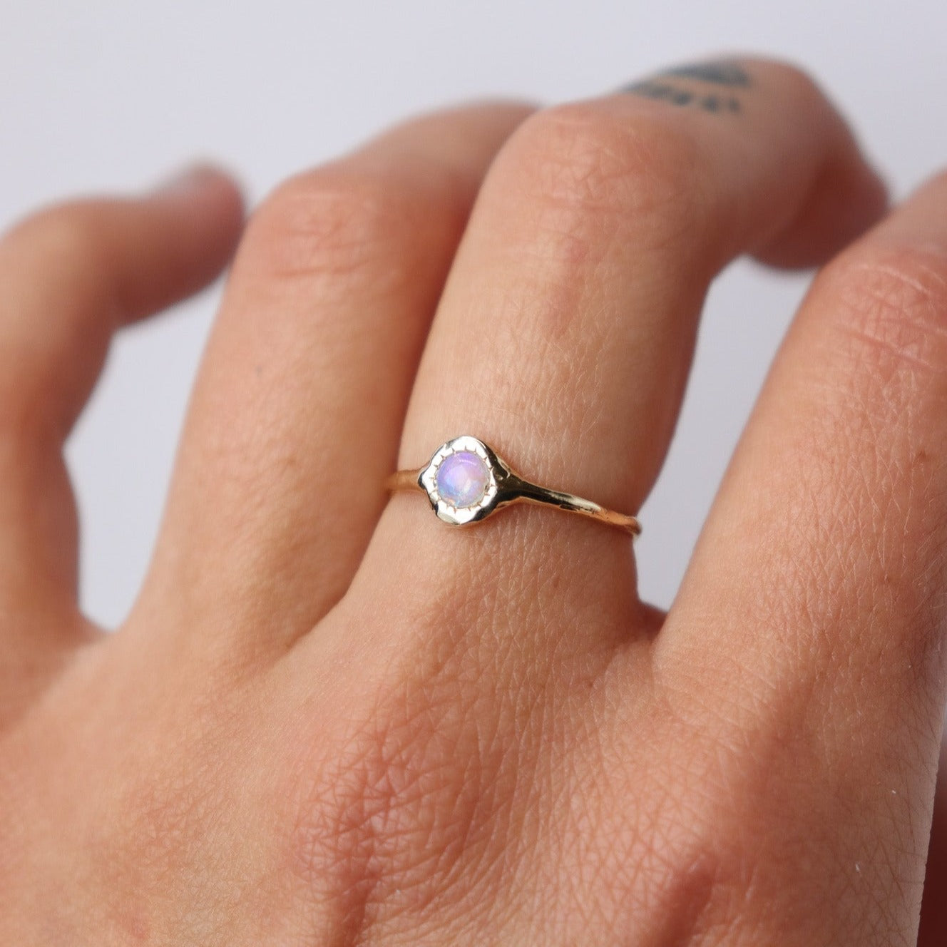 Unique round opal ring, set on a slender band with small tick-like accents that radiate like a starburst, creating a mesmerizing and celestial jewelry piece, worn on a hand to showcase scale.