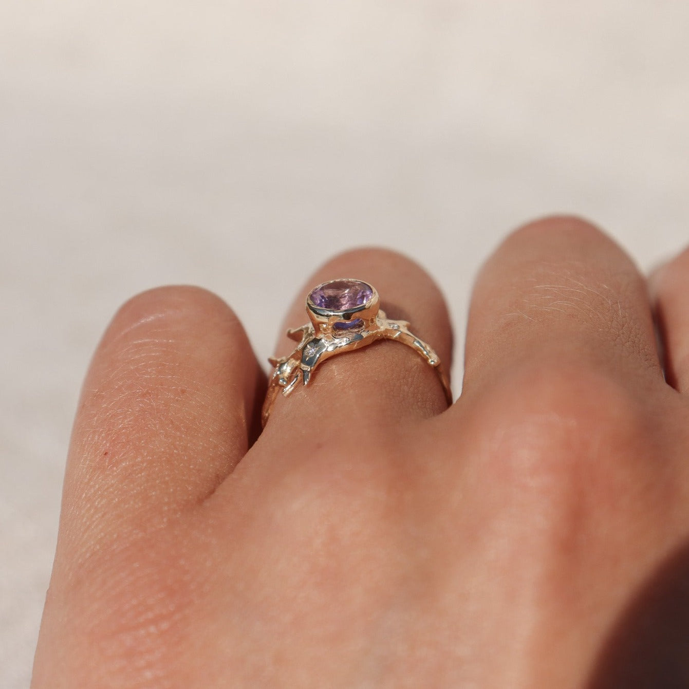 Exquisite round brilliant cut ametrine gemstone, bezel-set in a gold band with an organic coral-like design, adorned with sparkling diamond accents, shown from the side to depict the cut outs under the gem.