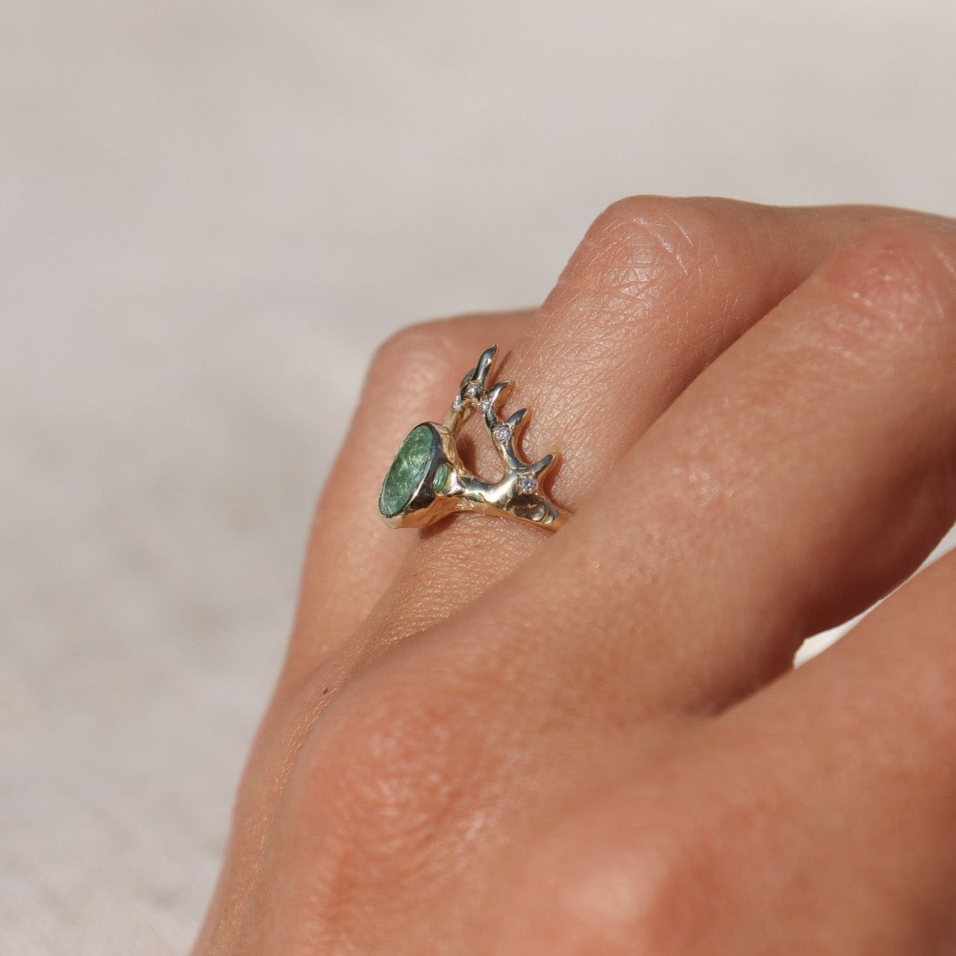 Side view of  an elegant oval Paraiba tourmaline bezel-set in a coral-inspired crown-like V-shaped gold setting, accentuated by sparkling diamond details