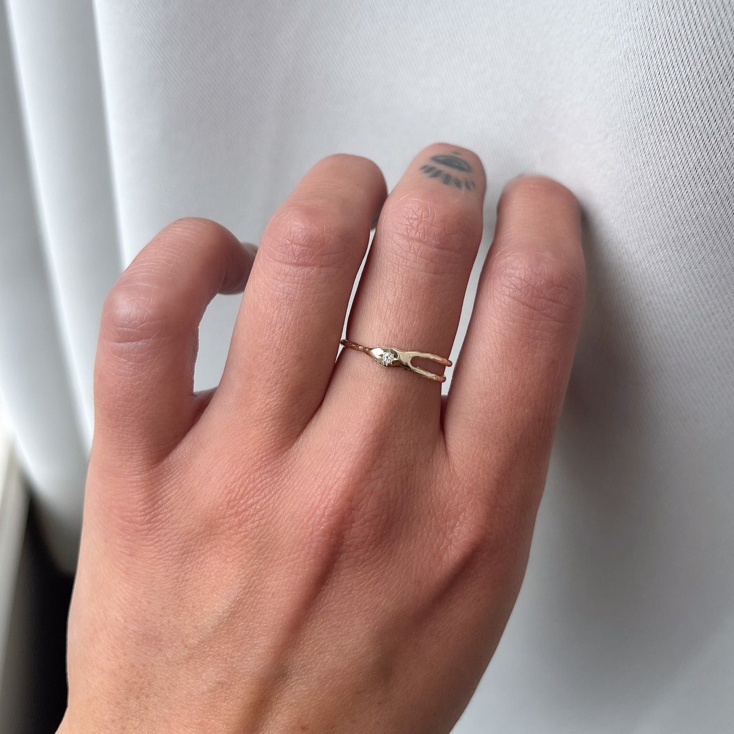 Asymmetrical gold ring with split band centered around a star-set diamond, resembling a shooting star for a unique and celestial design, worn to show scale.