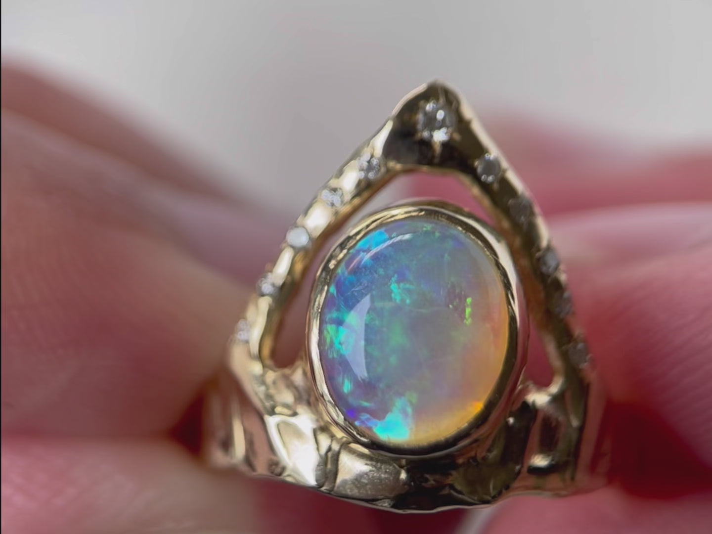 Stunning ring featuring a bezel-set opal on a wide, organically shaped band, adorned with a crown-like V-shaped band encircling the opal and embellished with glistening diamond accents