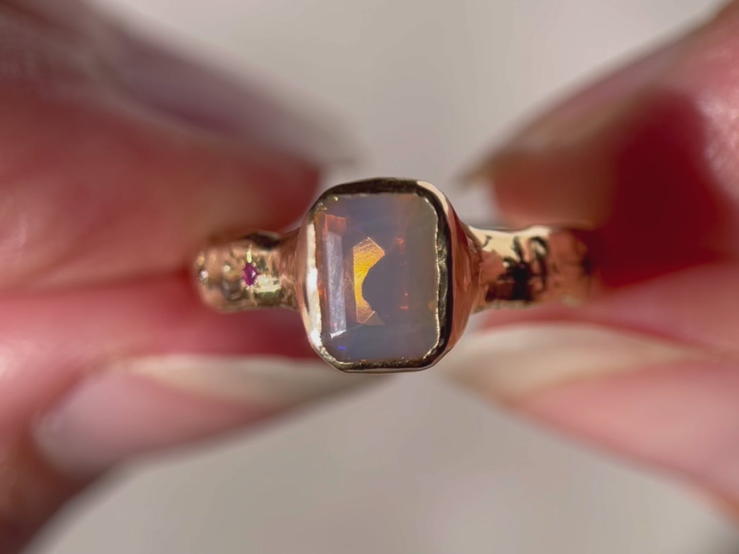 A close up video of an emerald cut opal is bezel set in 14k gold with a wide band that features ombre sapphires star set a long each side of the band.