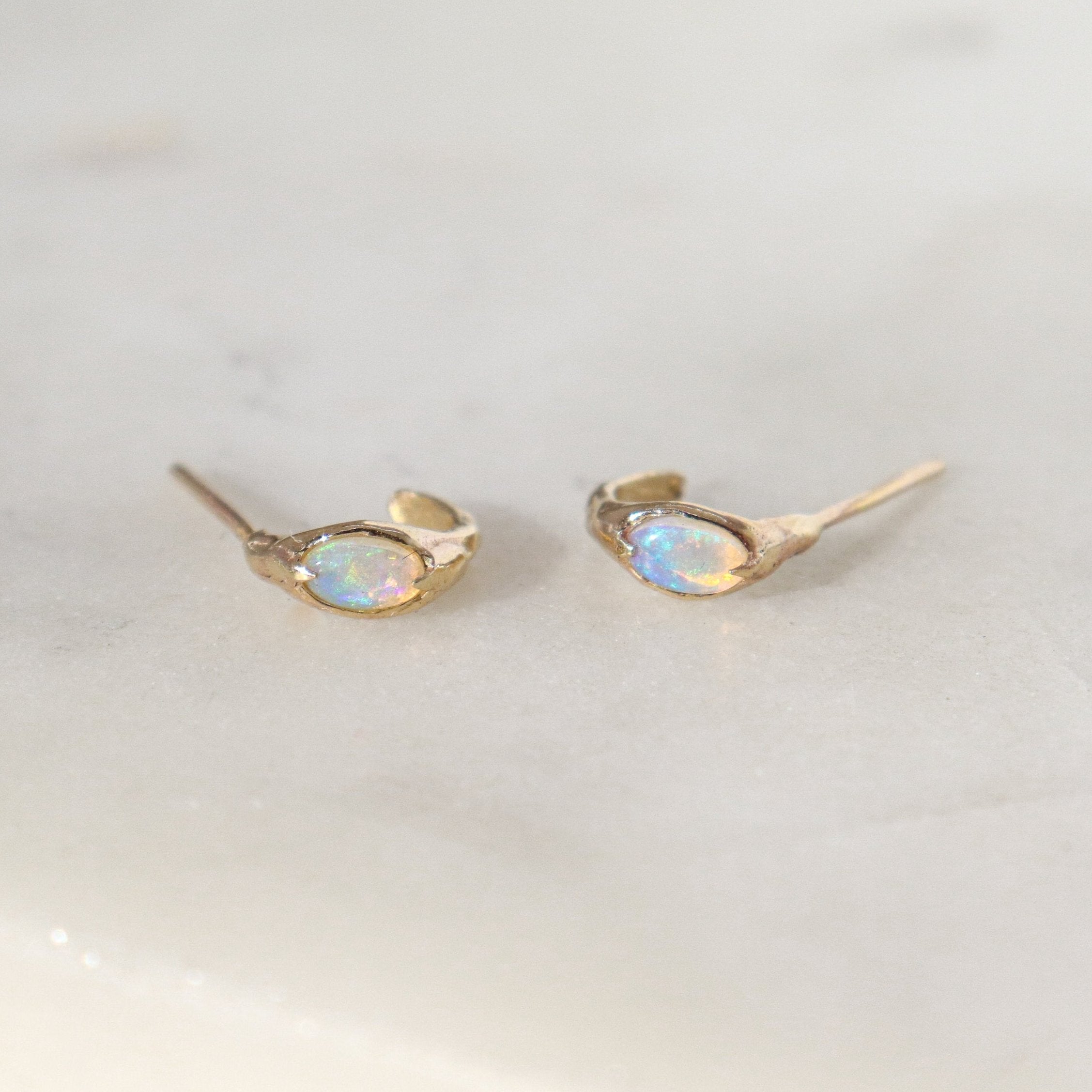 A pair of opal huggie hoops laid on their side on a white surface