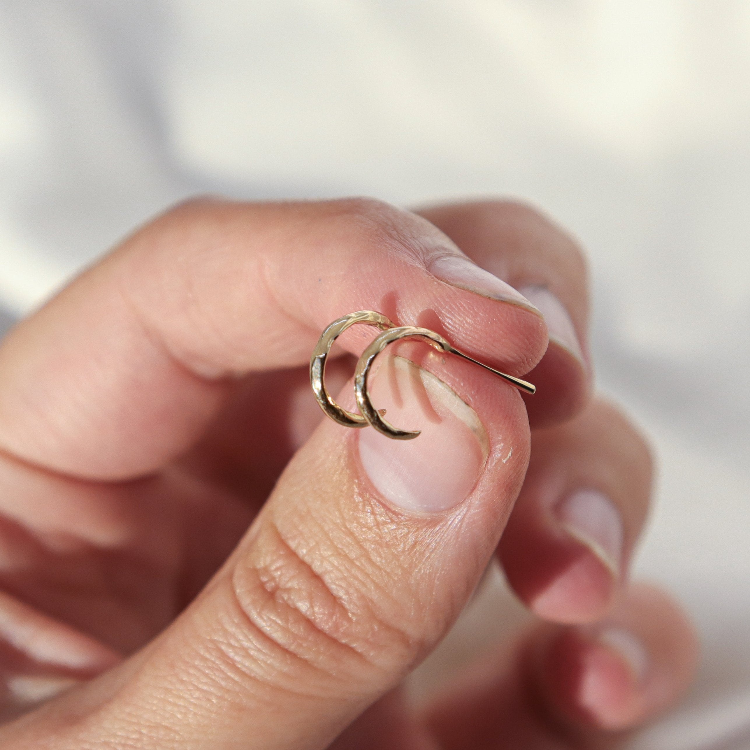 A hand holding a pair of plain huggie hoops to show the side view