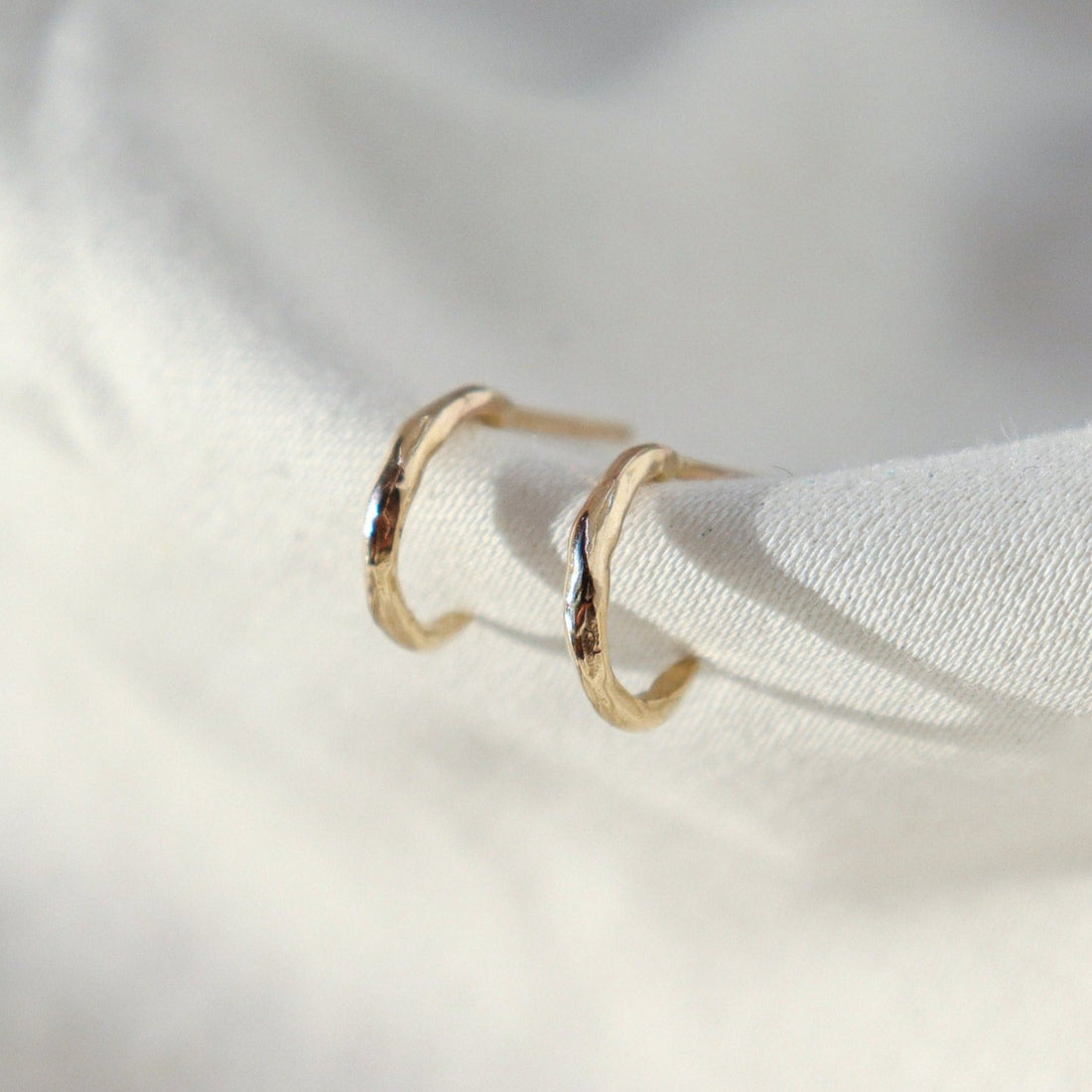 A pair of classic huggie hoops positioned on white fabric