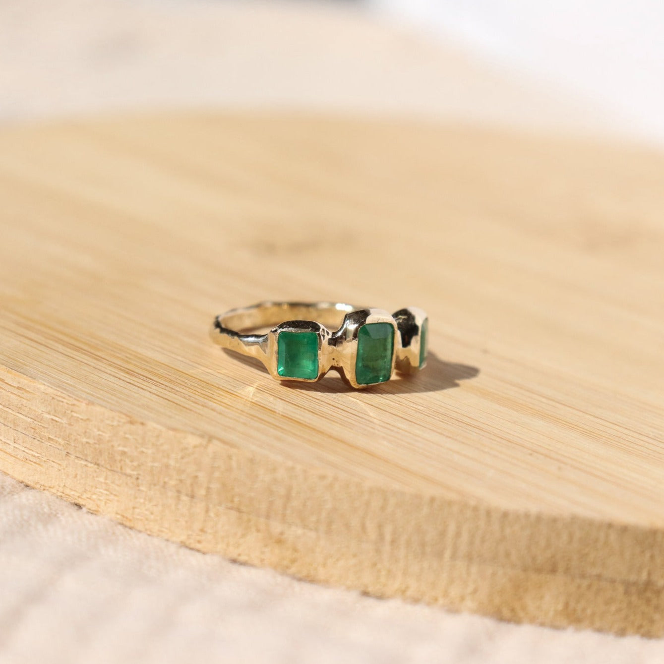 side view of a trio emerald ring positioned on a wood surface