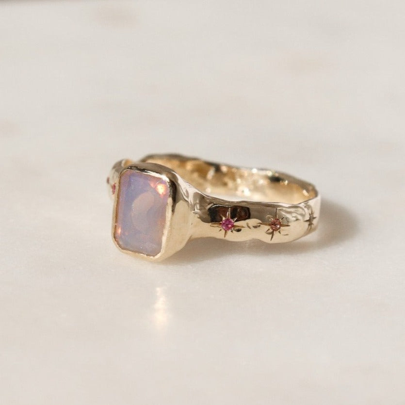 An emerald cut opal is bezel set in 14k gold with a wide band that features ombre sapphires star set a long each side of the band.