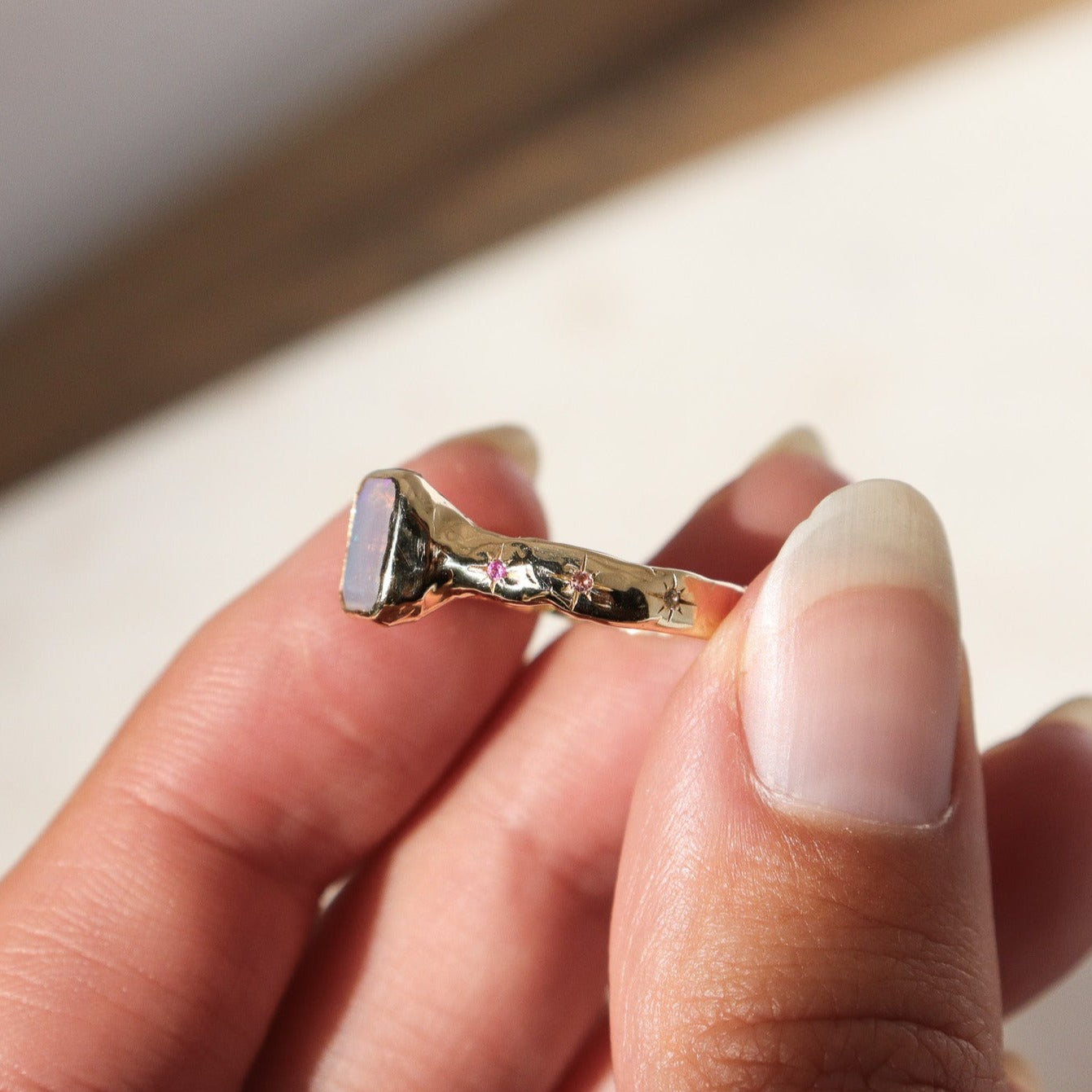 An emerald cut opal is bezel set in 14k gold with a wide band that features ombre sapphires star set a long each side of the band.