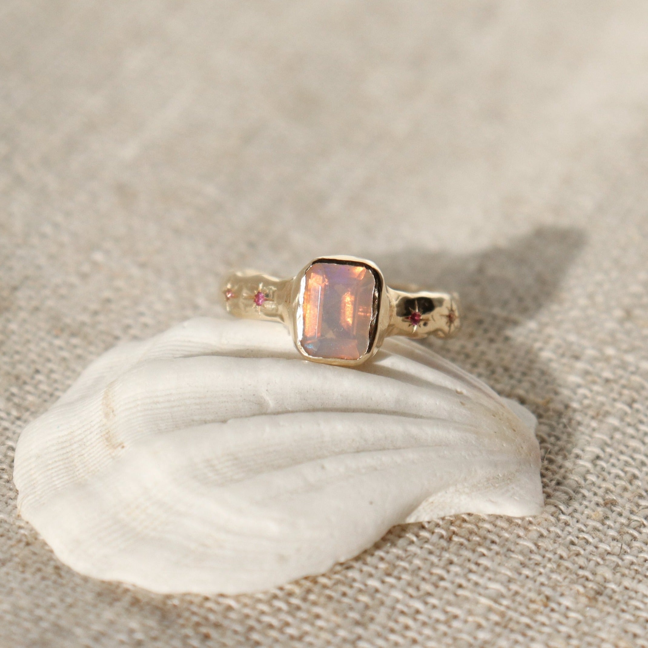 An emerald cut opal is bezel set in 14k gold with a wide band that features ombre sapphires star set a long each side of the band.