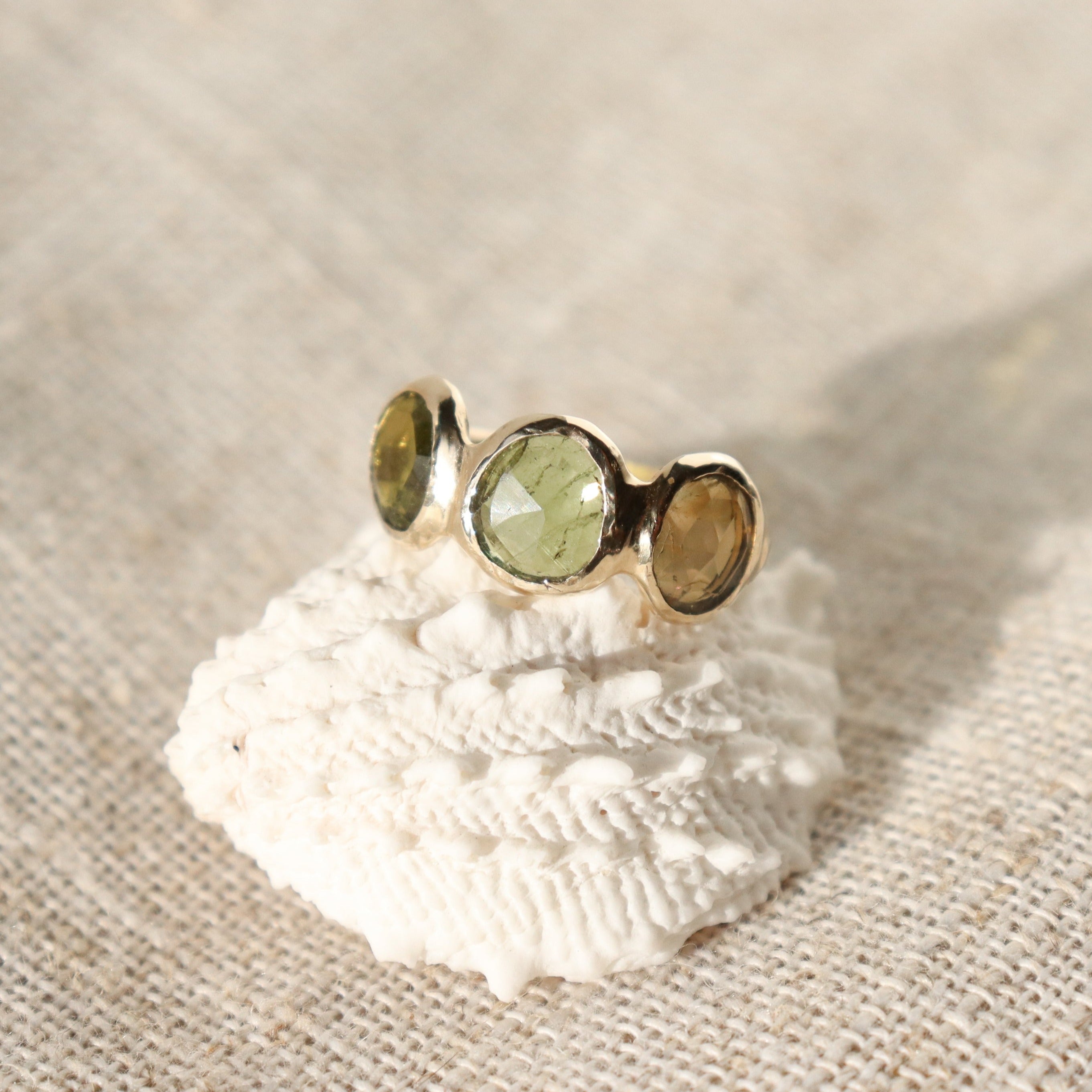 Three rose cut green tourmaline stones are bezel set in 14k gold along an organic band.