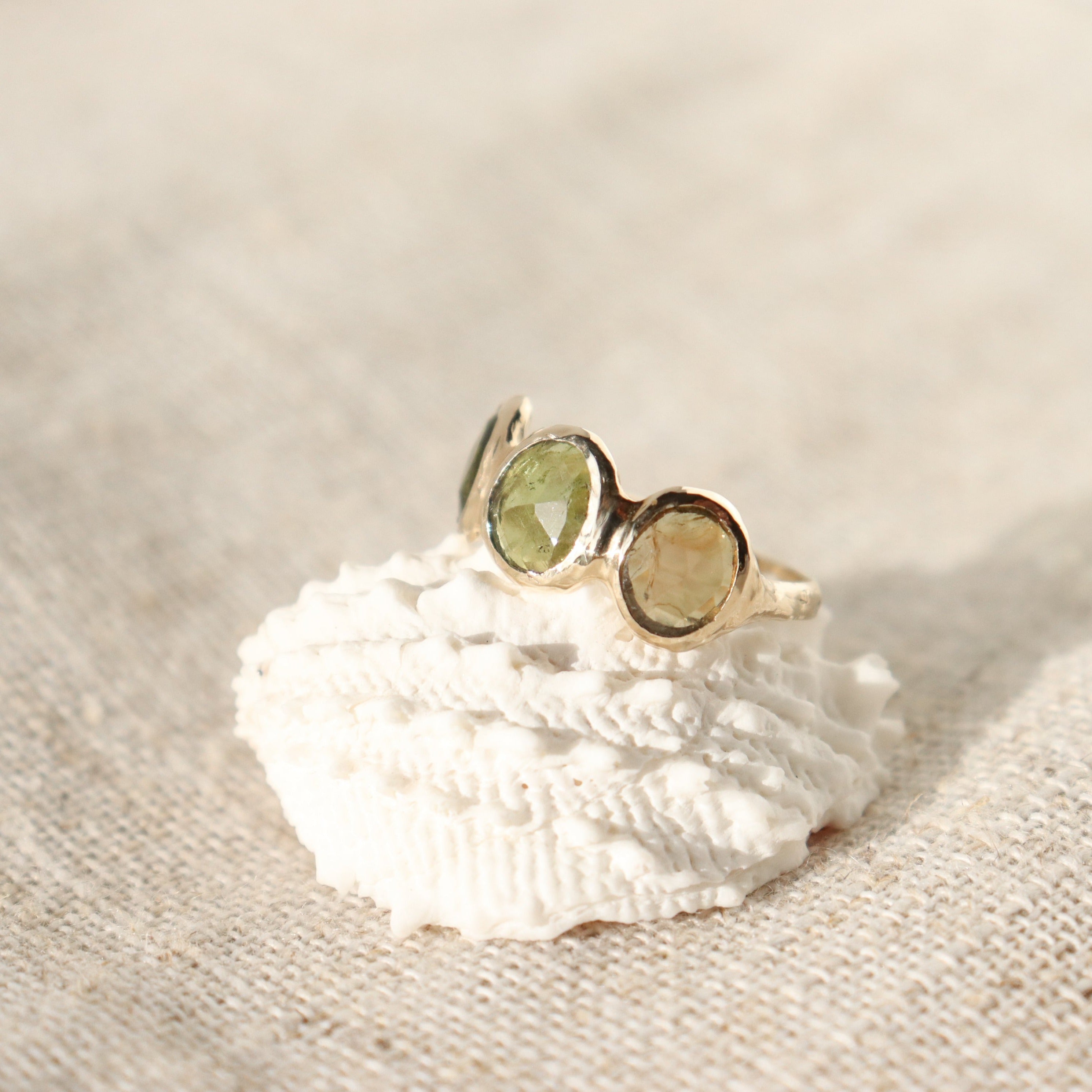 Three rose cut green tourmaline stones are bezel set in 14k gold along an organic band.