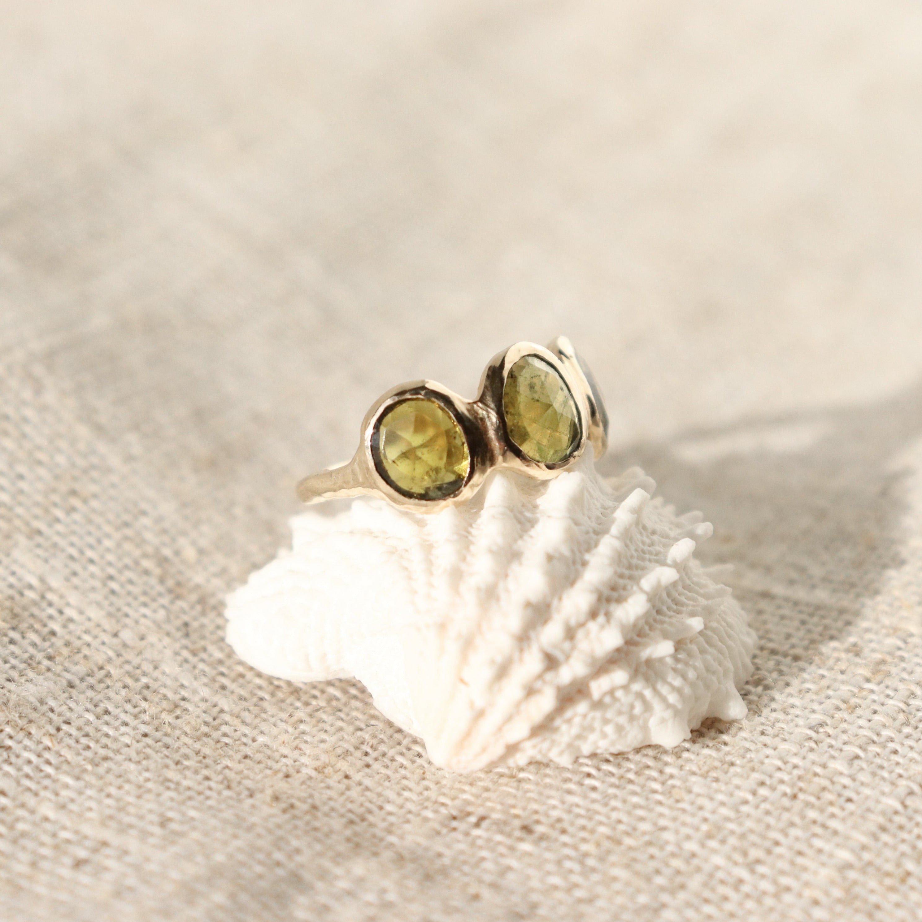 Three rose cut green tourmaline stones are bezel set in 14k gold along an organic band.