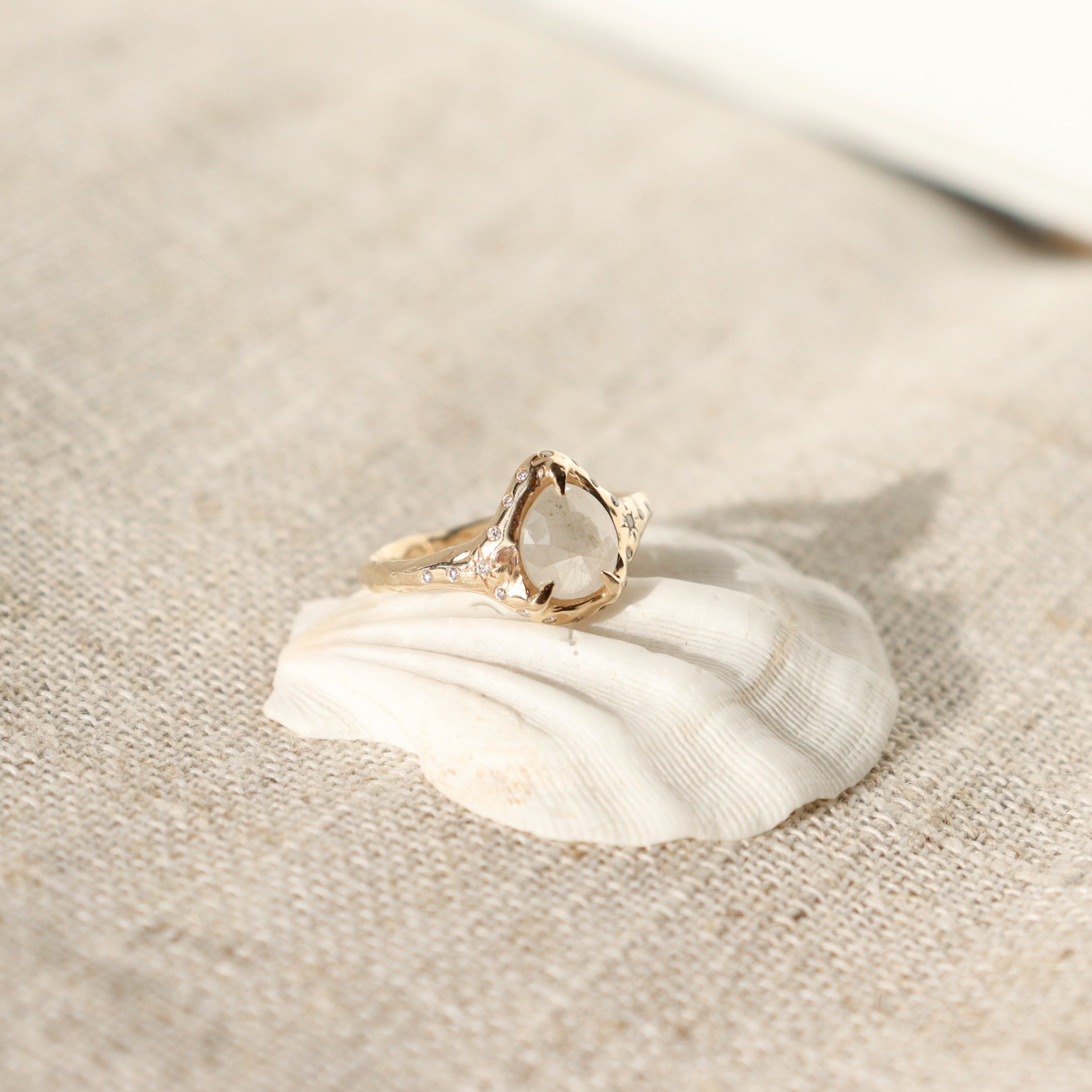 A pear shaped icy diamond is set with prongs and surrounded by diamonds on a 14k gold band.