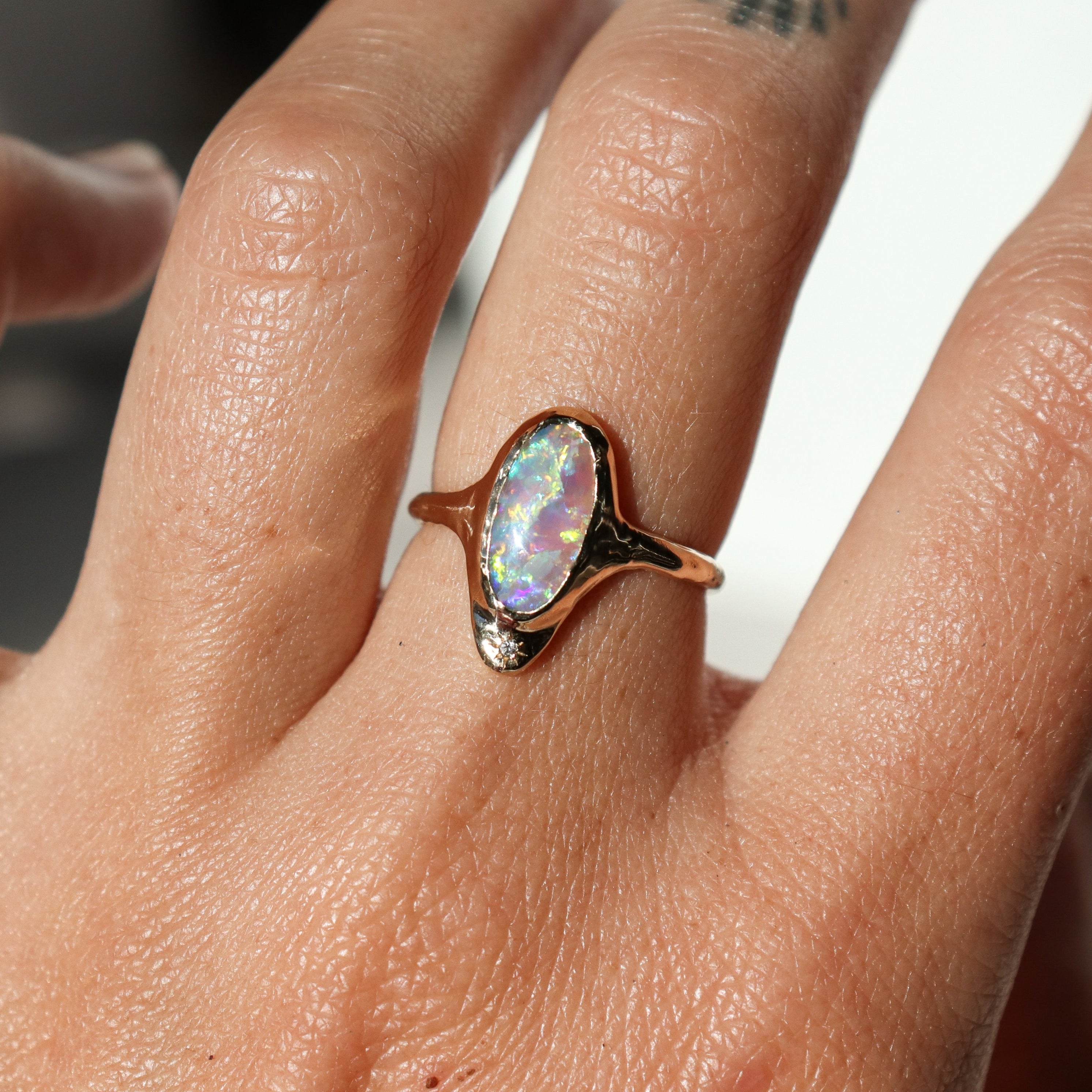 A long oval opal is bezel set in 14k gold  with  a star set  diamond at the base of the ring.