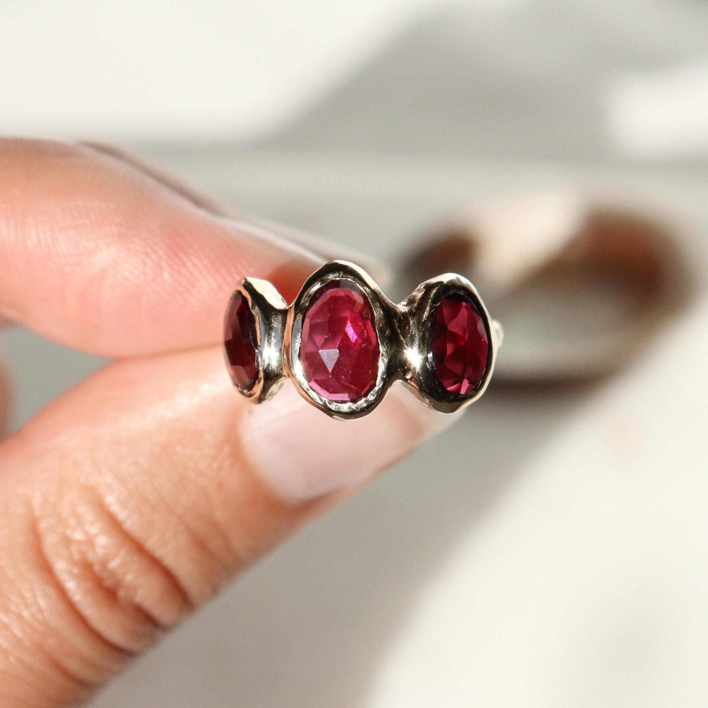 Three rose cut rhodolite garnets are bezel set on an organically crafted 14k gold band.