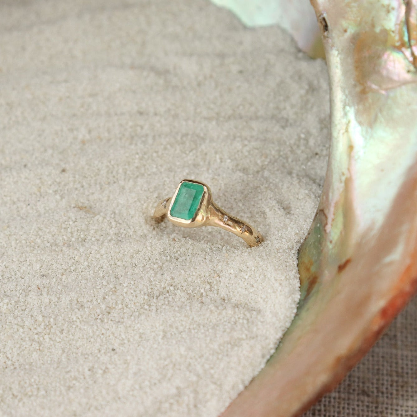 An emerald cut emerald ring is bezel set in 14k gold with a wide band that has multiple star set diamonds along the sides.