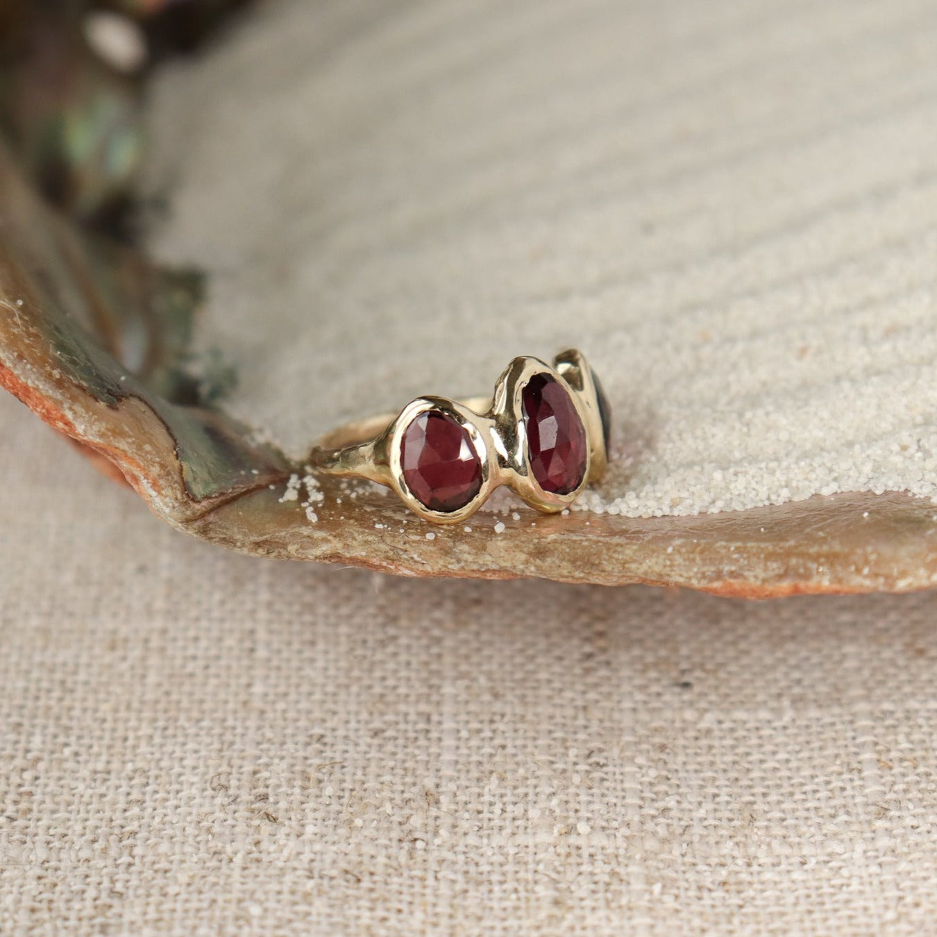 Three rose cut rhodolite garnets are bezel set on an organically crafted 14k gold band.