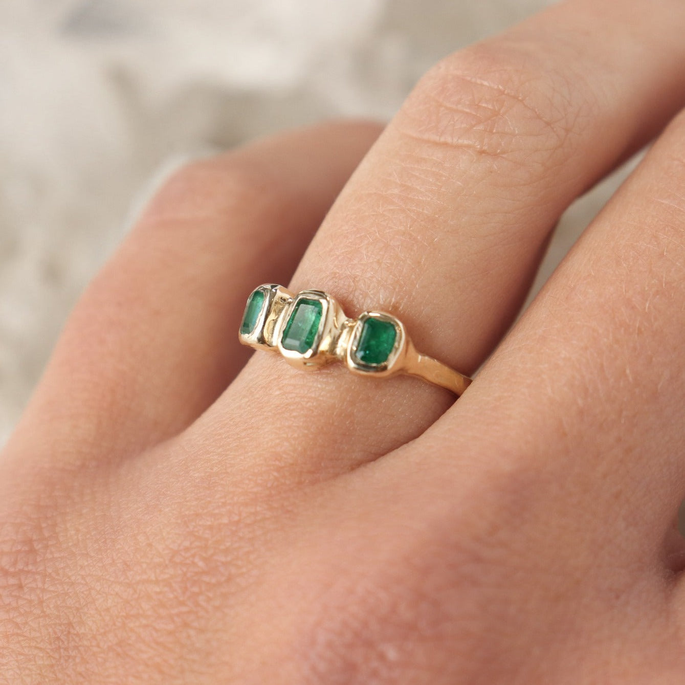 Three small emerald cut emeralds are embedded into a 14k gold ring giving it an organic and handcrafted look.