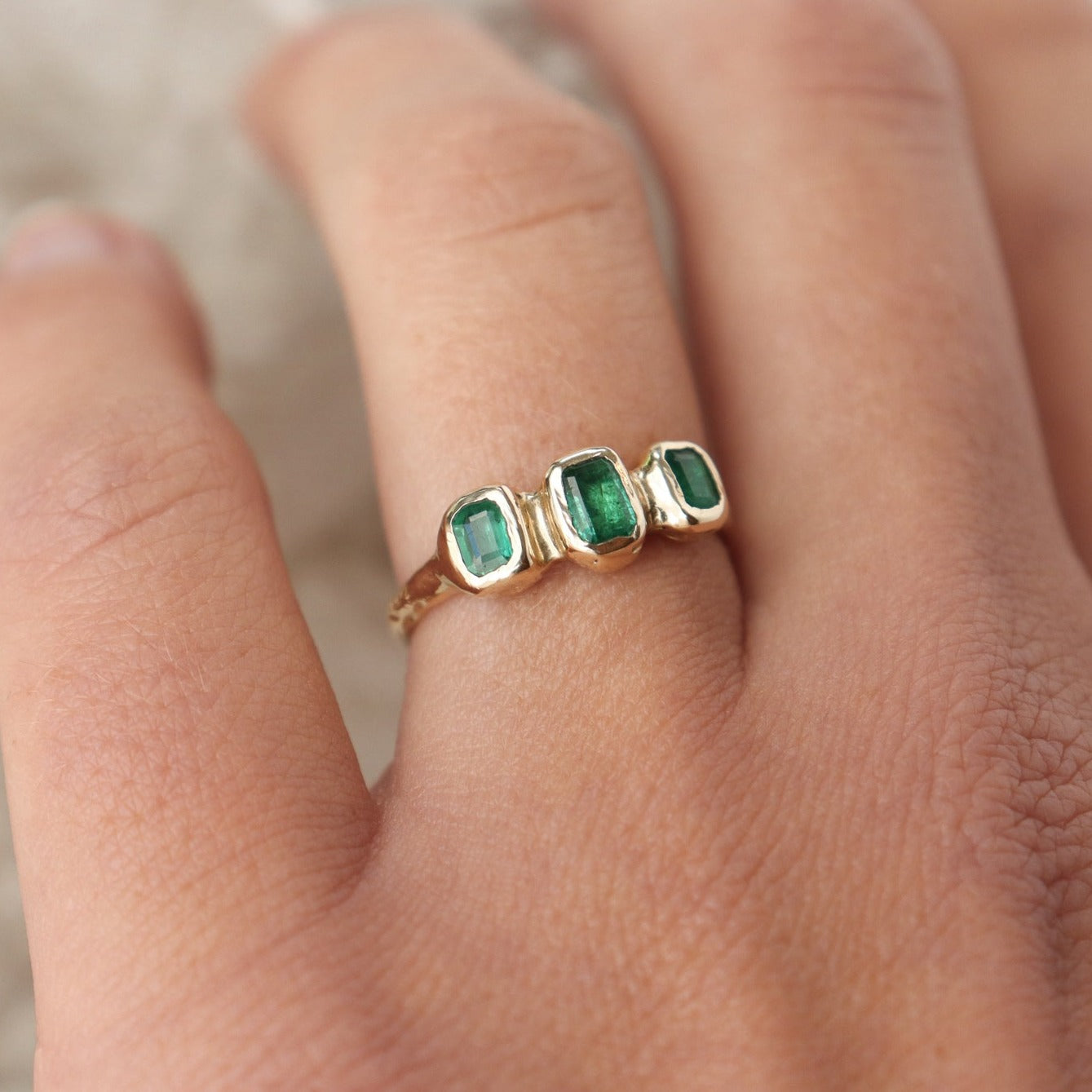 Worn on the ring finger, three small emerald cut emeralds are embedded into a 14k gold ring giving it an organic and handcrafted look.