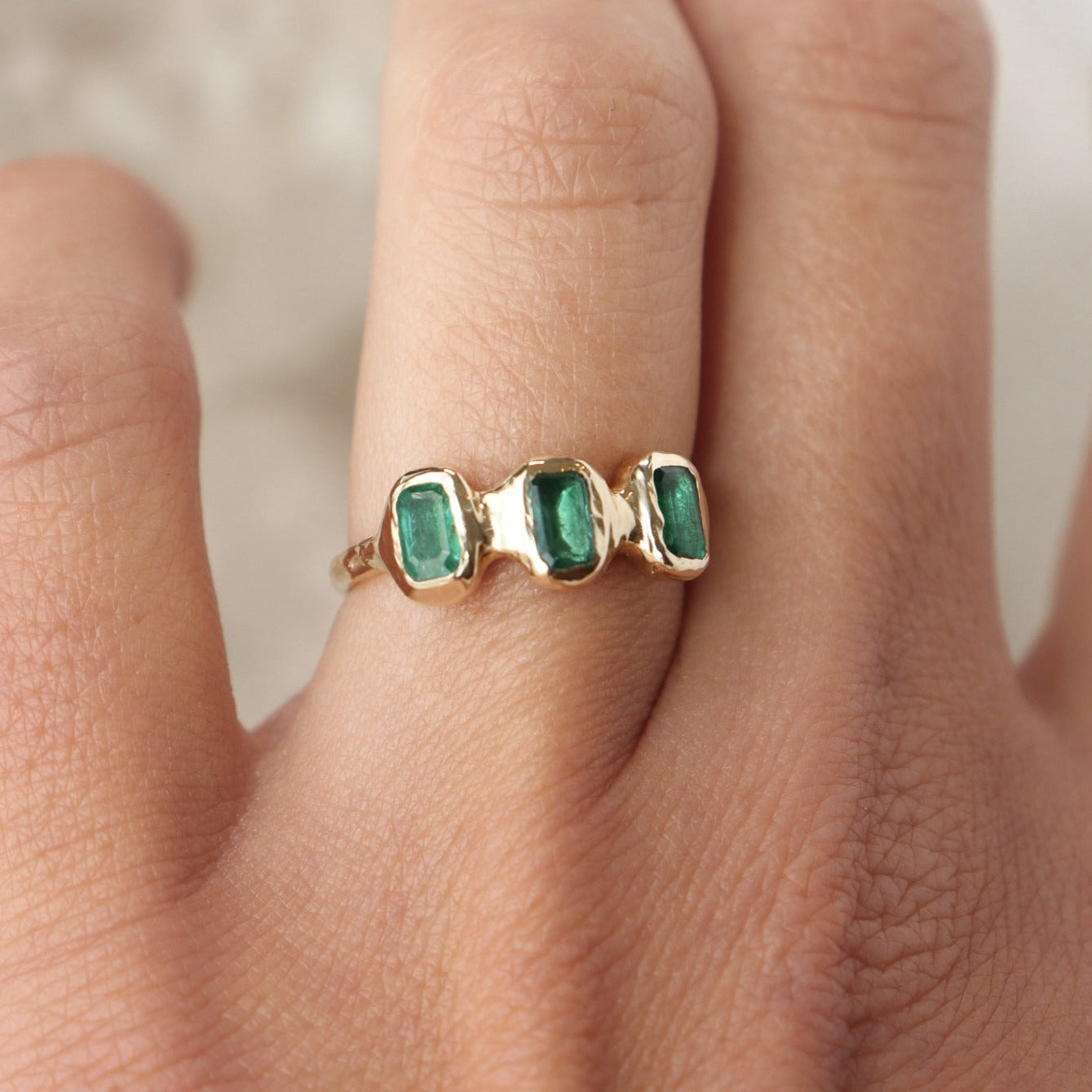 Three small emerald cut emeralds are embedded into a 14k gold ring giving it an organic look.