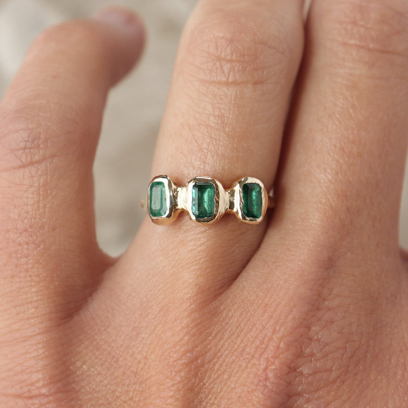 Three small emerald cut emeralds are embedded into a 14k gold ring giving it an organic look.