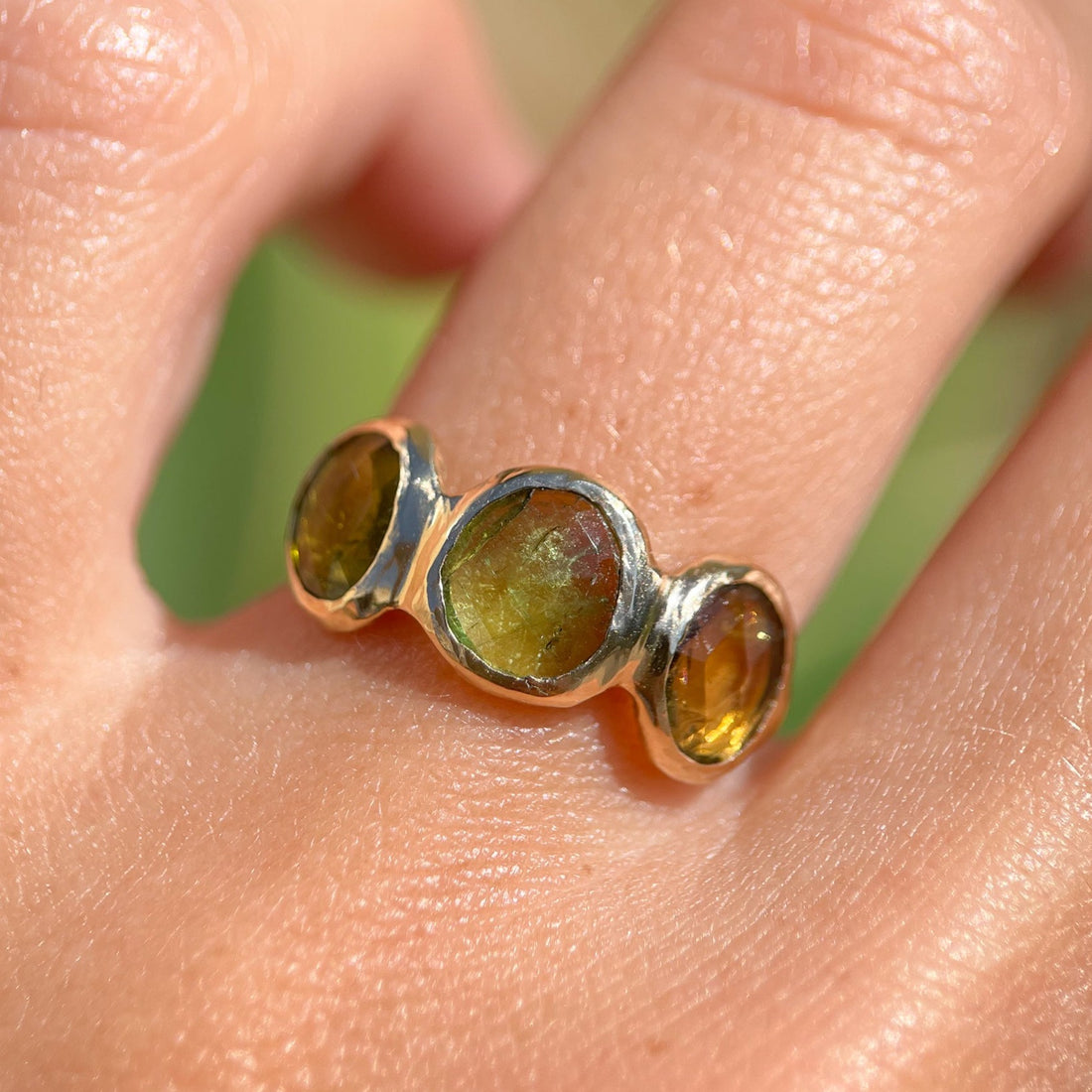 Three rose cut green tourmaline stones are bezel set in 14k gold along an organic band.