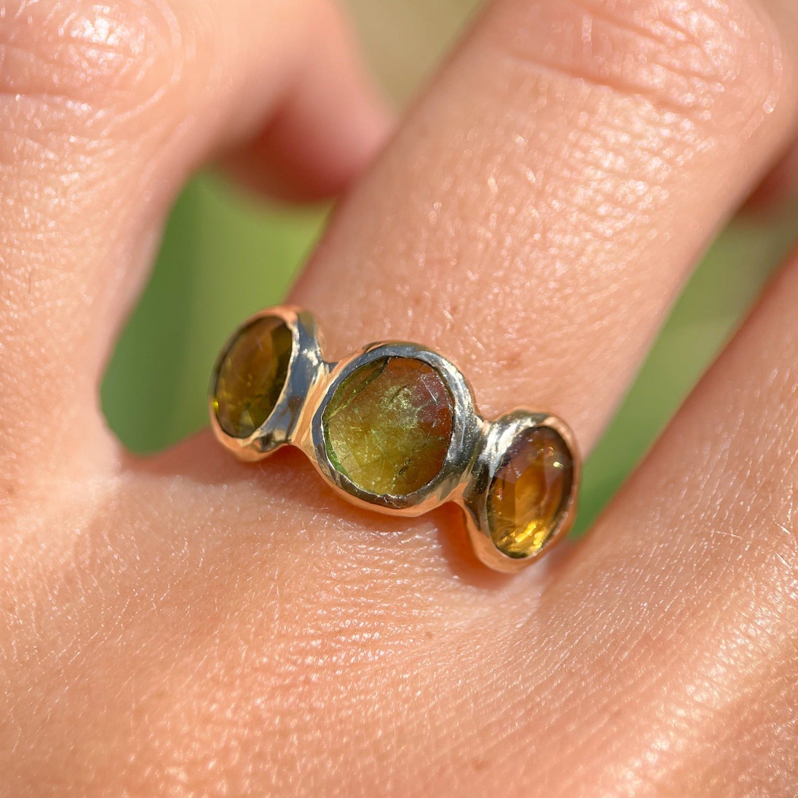 Three rose cut green tourmaline stones are bezel set in 14k gold along an organic band.