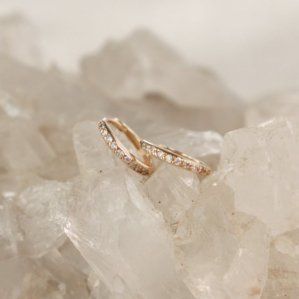 A pair of 14k gold huggie hoops with diamonds pave set along the front.