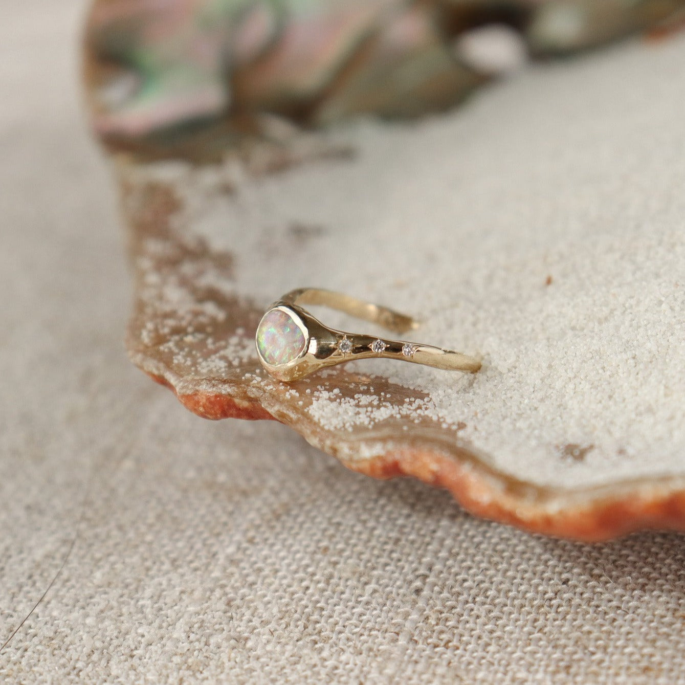 Side view of a crystal boulder opal that is bezel set on an  organically crafted band with three star set diamonds on each side of the stone.