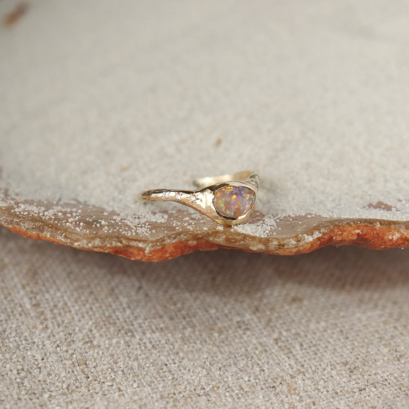 Side view of a crystal boulder opal that is bezel set on an  organically crafted band with three star set diamonds on each side of the stone.