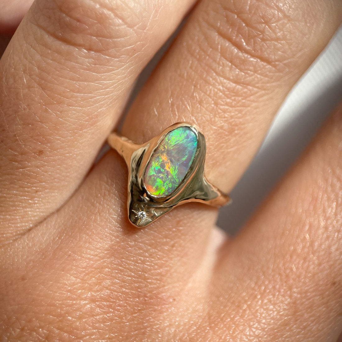 A long oval opal is bezel set in 14k gold with a star set diamond at the base of the ring.