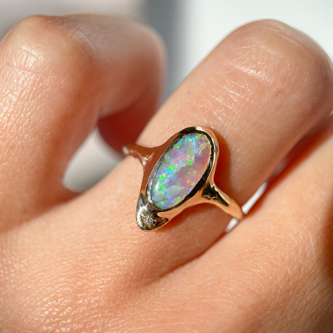 A long oval opal is bezel set in 14k gold with a star set diamond at the base of the ring.