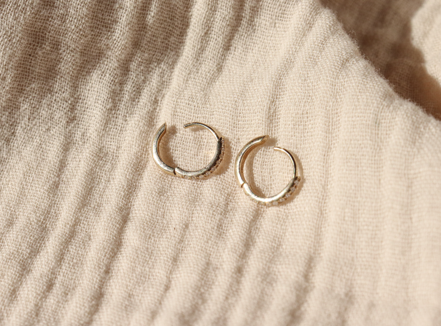 A pair of diamond pave hoops laid out flat and open to show how the hinge works
