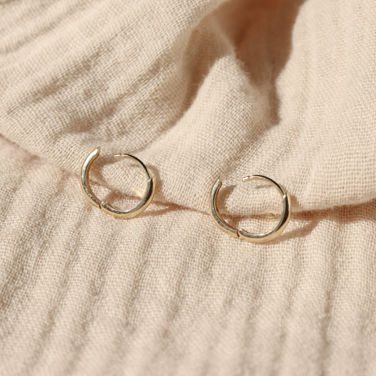 A pair of classic 14k gold hinge huggie hoops are laid out open to show how the hinge works