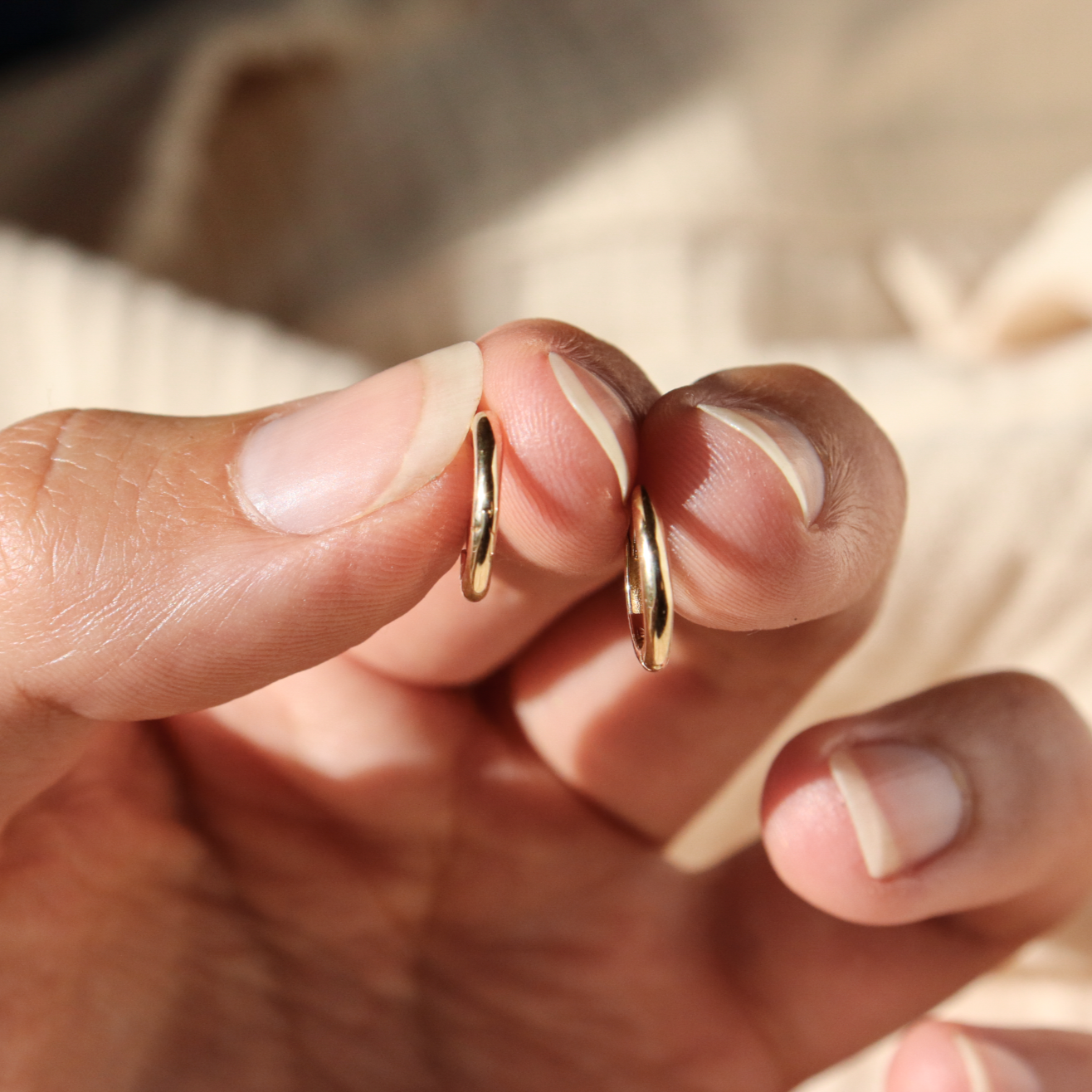Hand holding a pair of classic 14k gold hinge huggie hoops