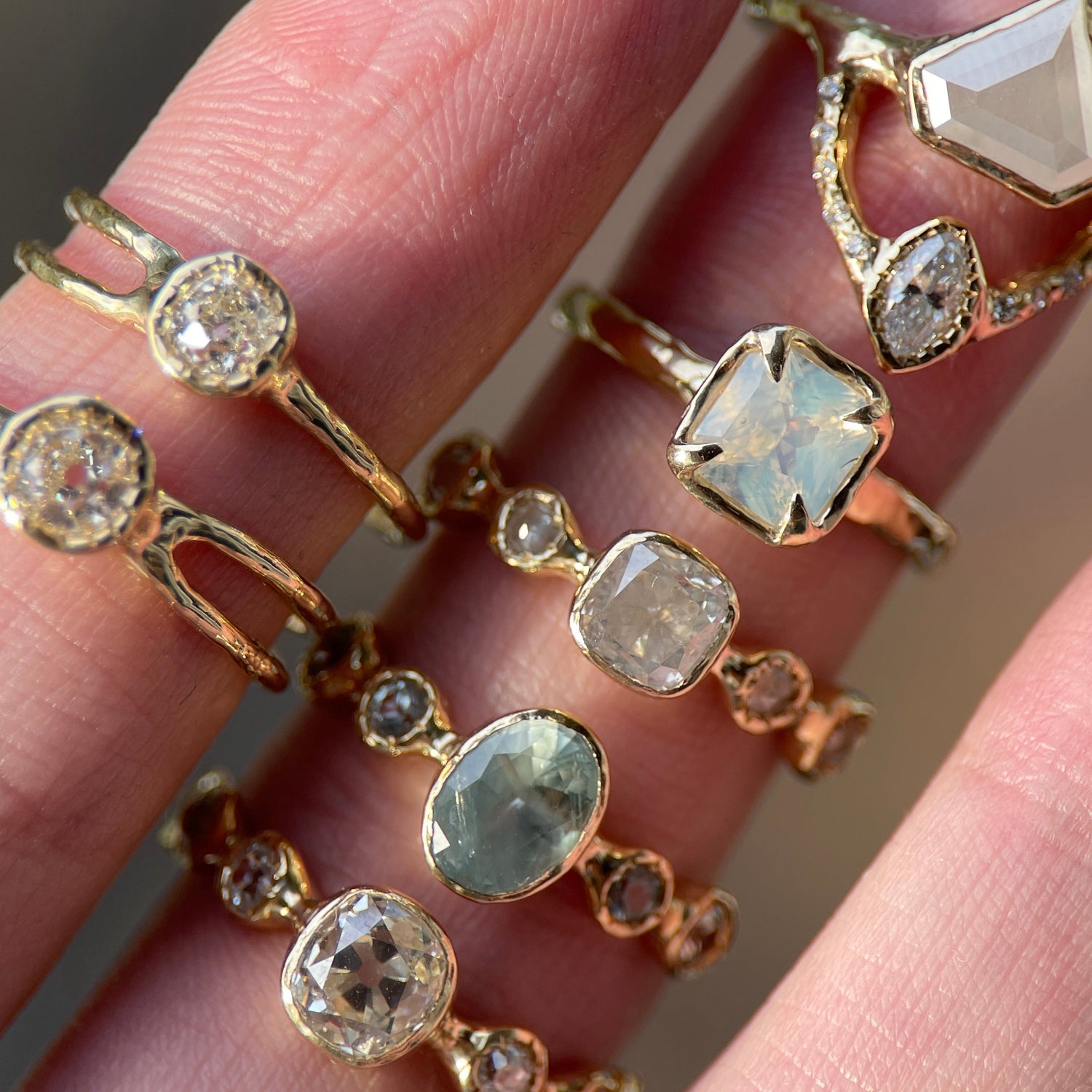 Gold rings with various gemstones on a hand against a blurred background