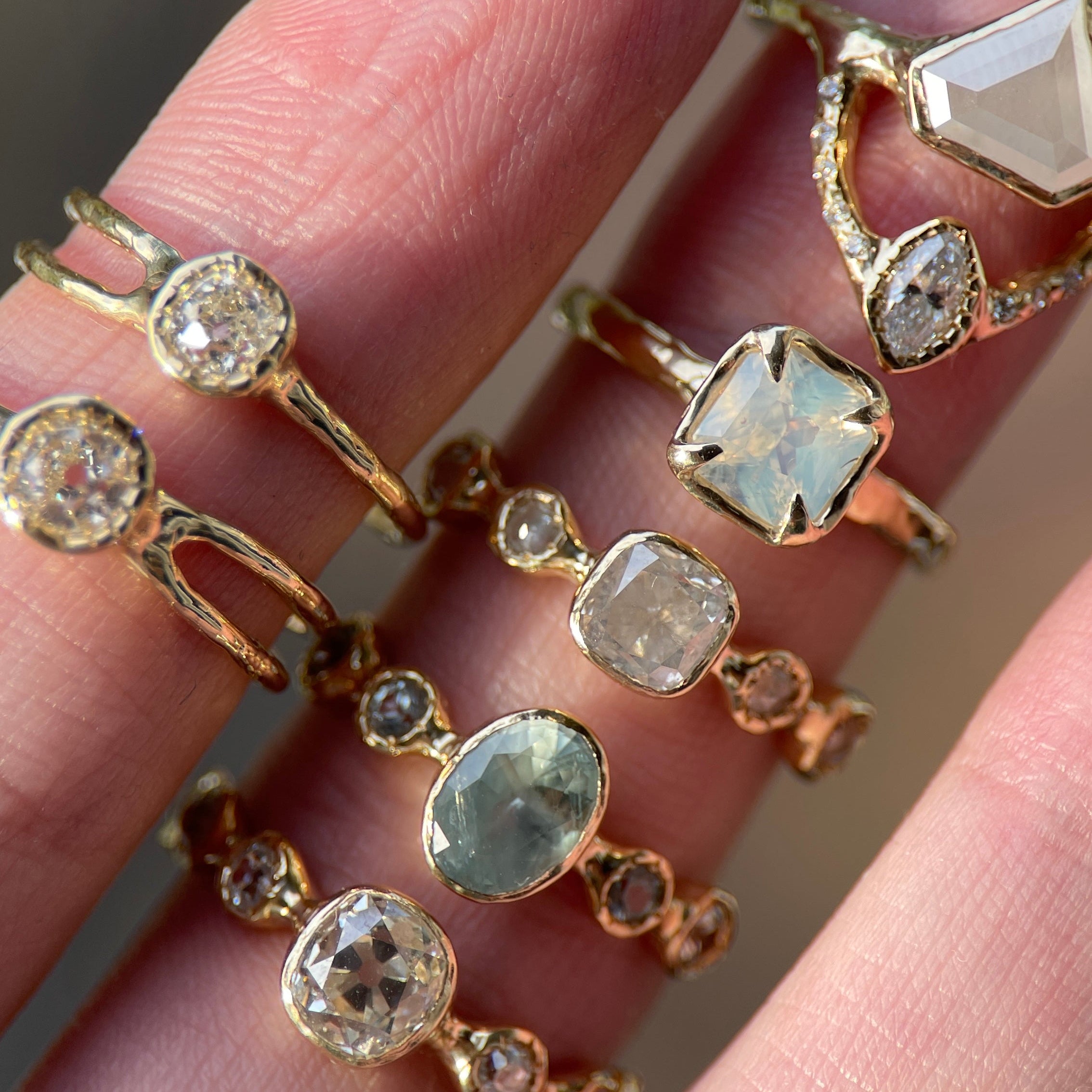 Gold rings with various gemstones on a hand against a blurred background