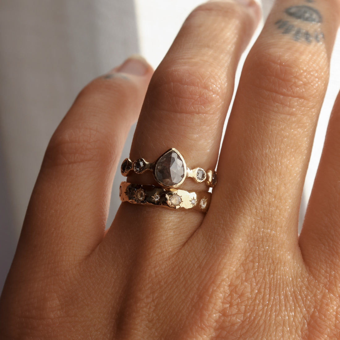 Hand wearing a stack of gold rings with gemstones on a neutral background