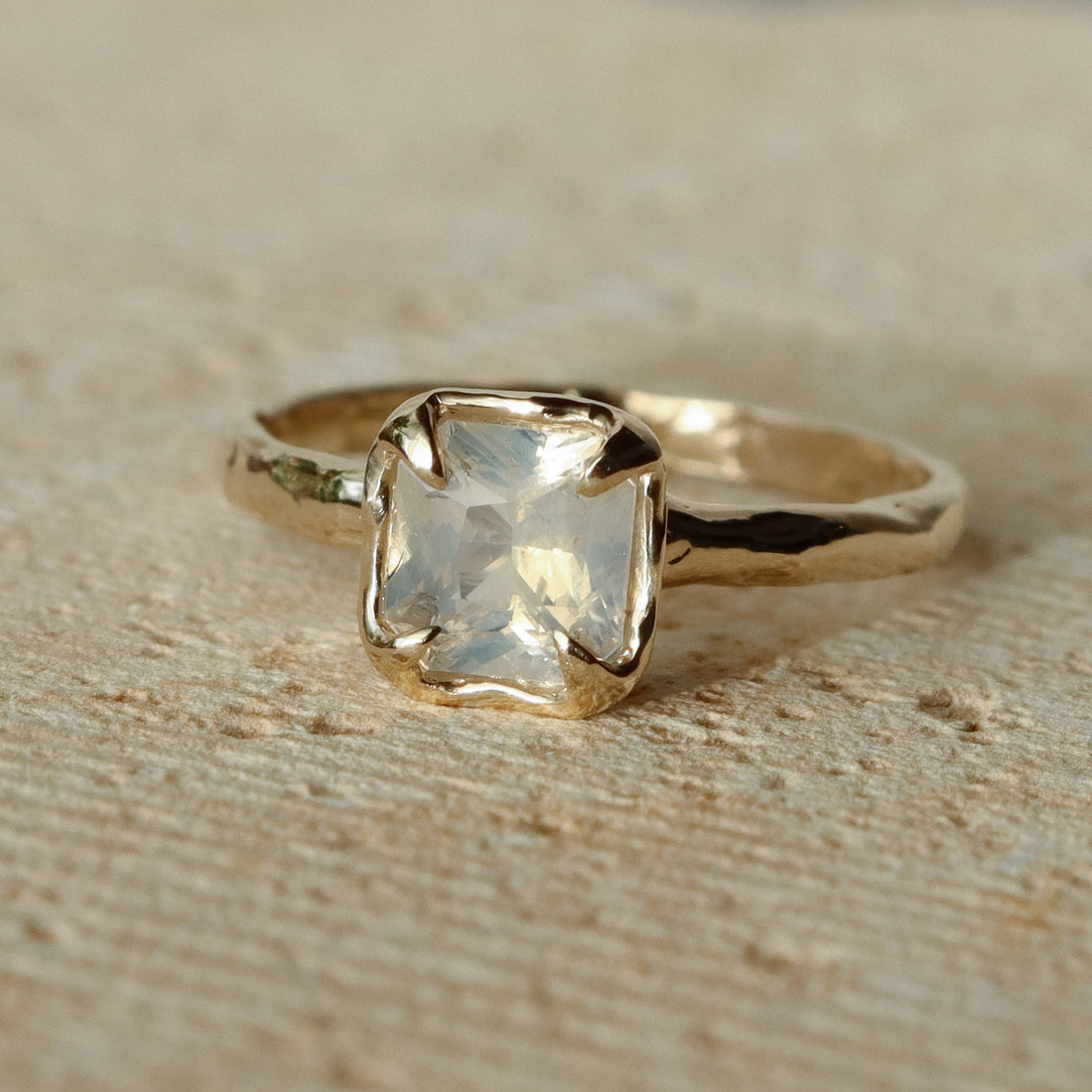 Gold ring with a clear gemstone on a beige surface
