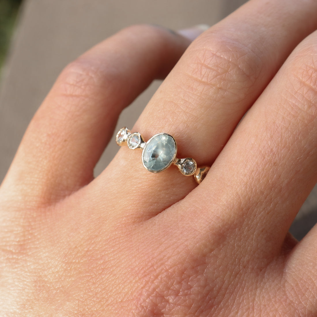 Close-up of a hand wearing a gold ring with a central blue gemstone and smaller stones.